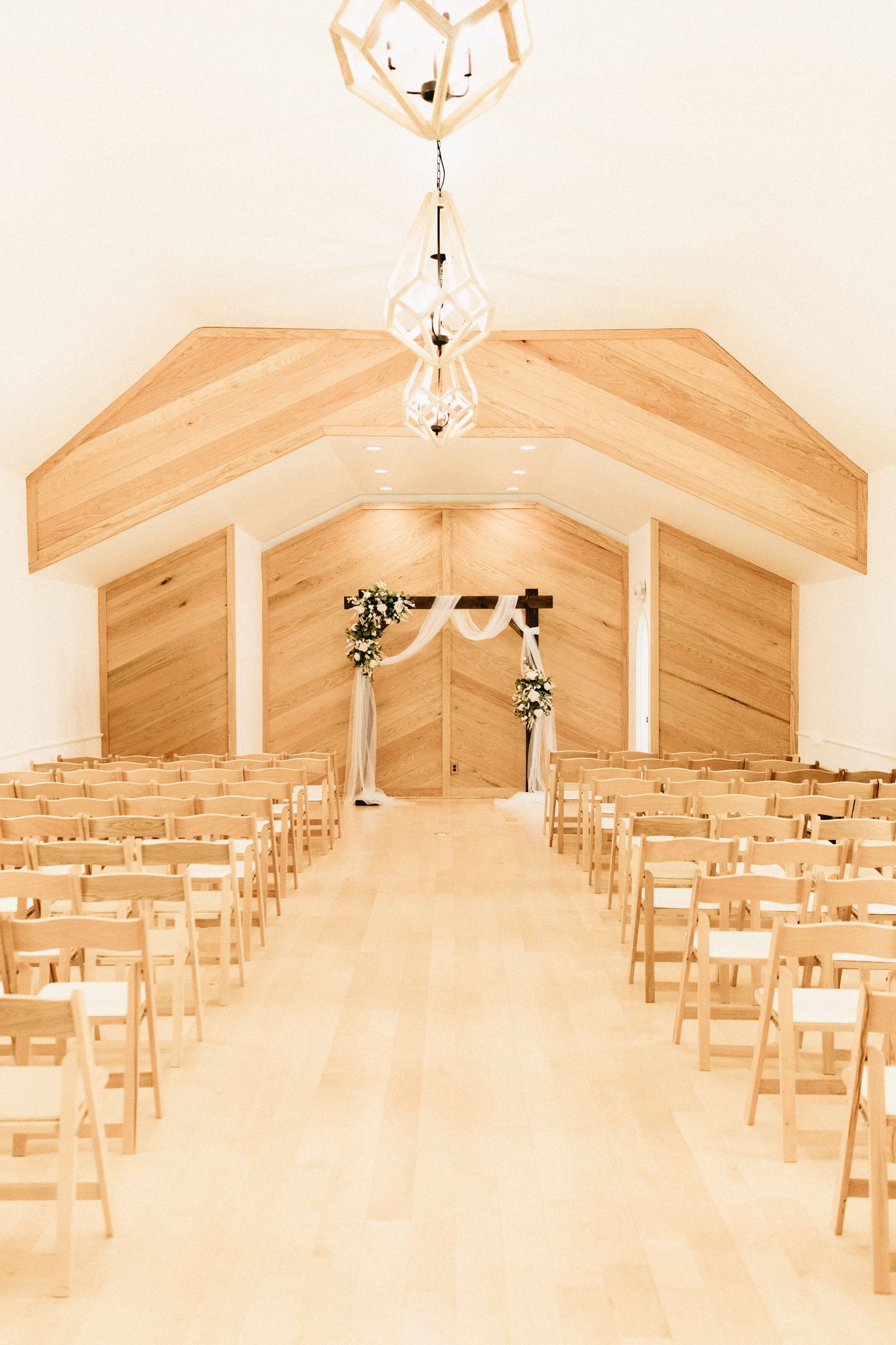 Interior of a modern chapel with wooden walls, vaulted ceiling, crystal chandeliers and rows of natural wood chairs for a wedding.