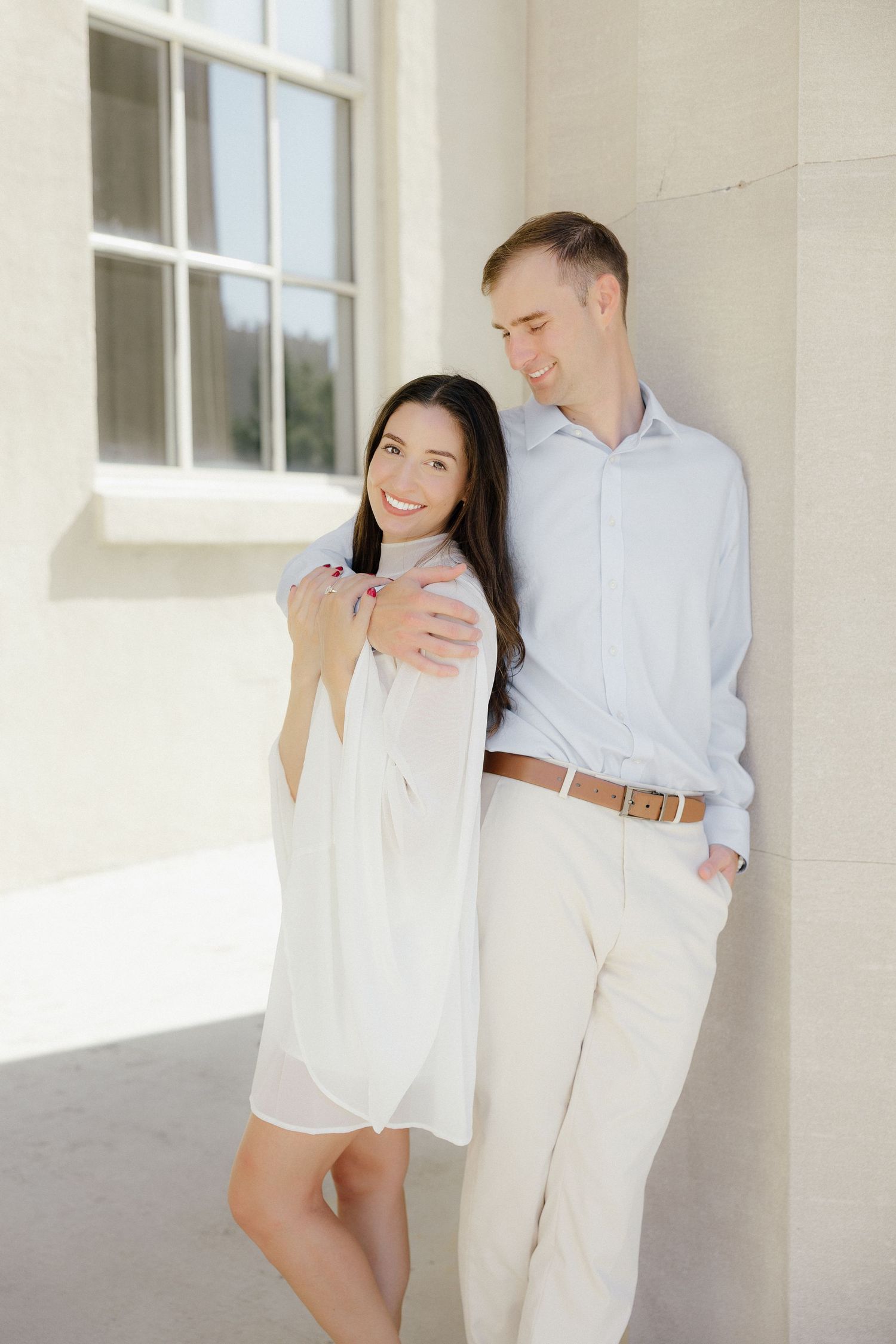 Affectionate couple leaning against a white stone column, smiling and embracing on a sunny day.