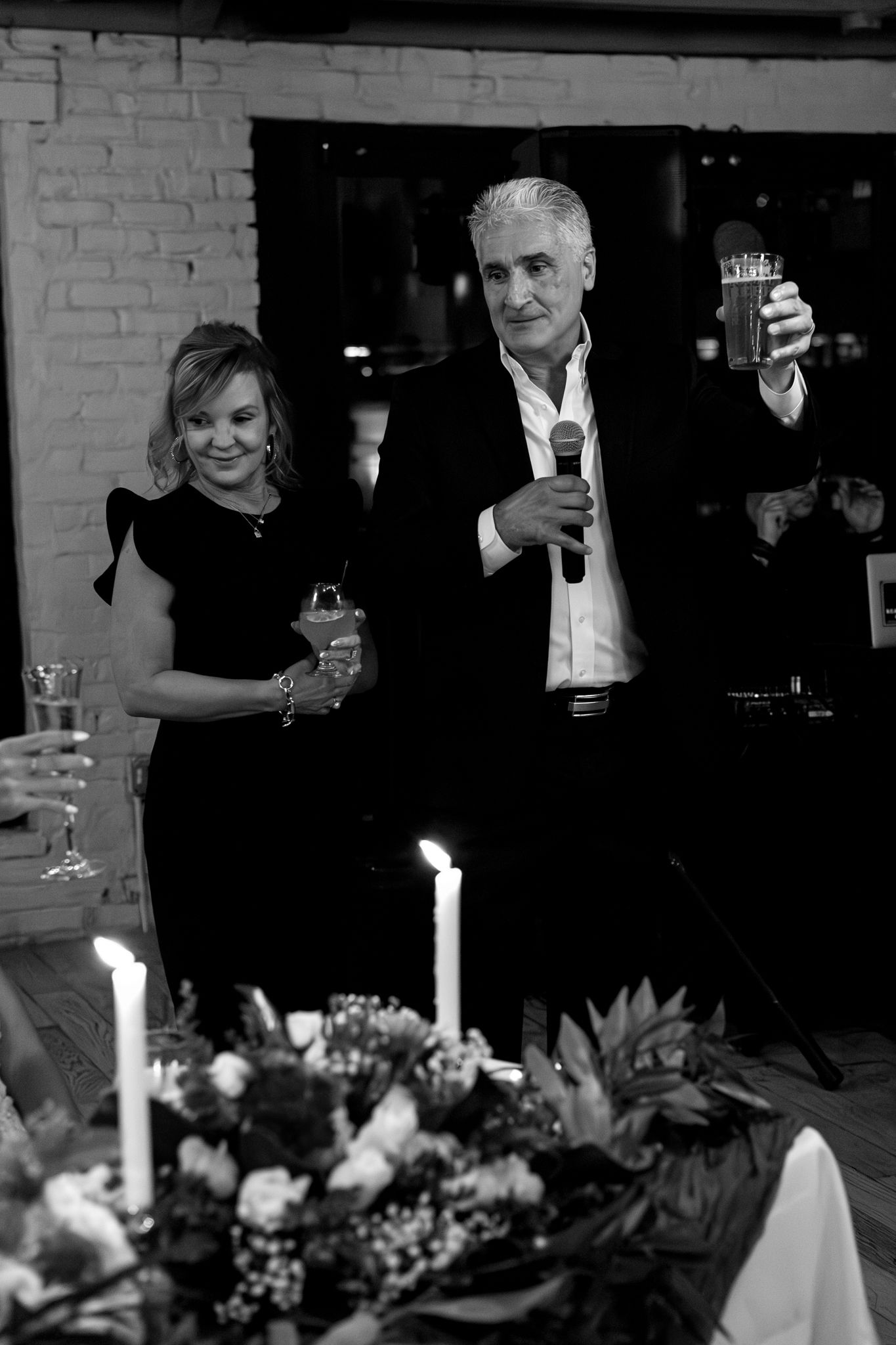 Elegant evening reception scene with guests making toasts beside floral centerpiece and candlelight.