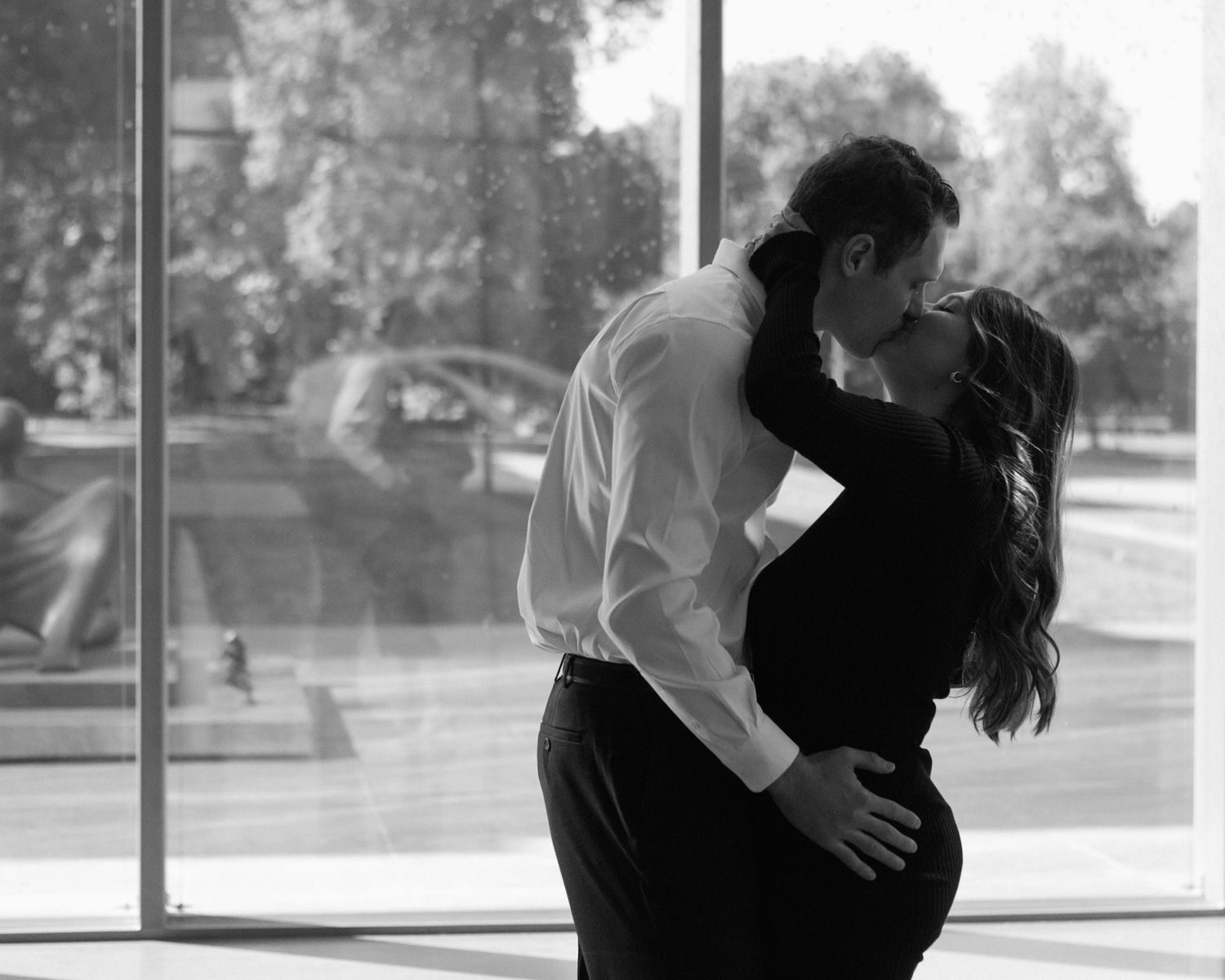 Engaged couple in downtown Louisville, with the woman smiling and showing her engagement ring while embracing her fiancé