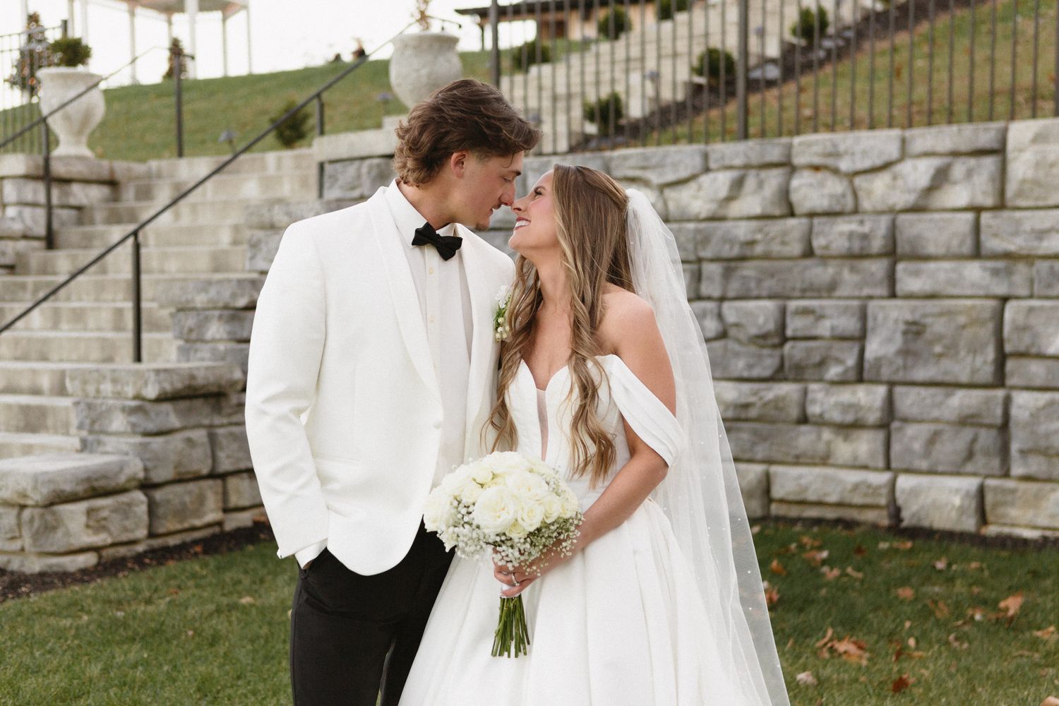 Bridal couple shares intimate moment by stone wall during outdoor fall wedding.