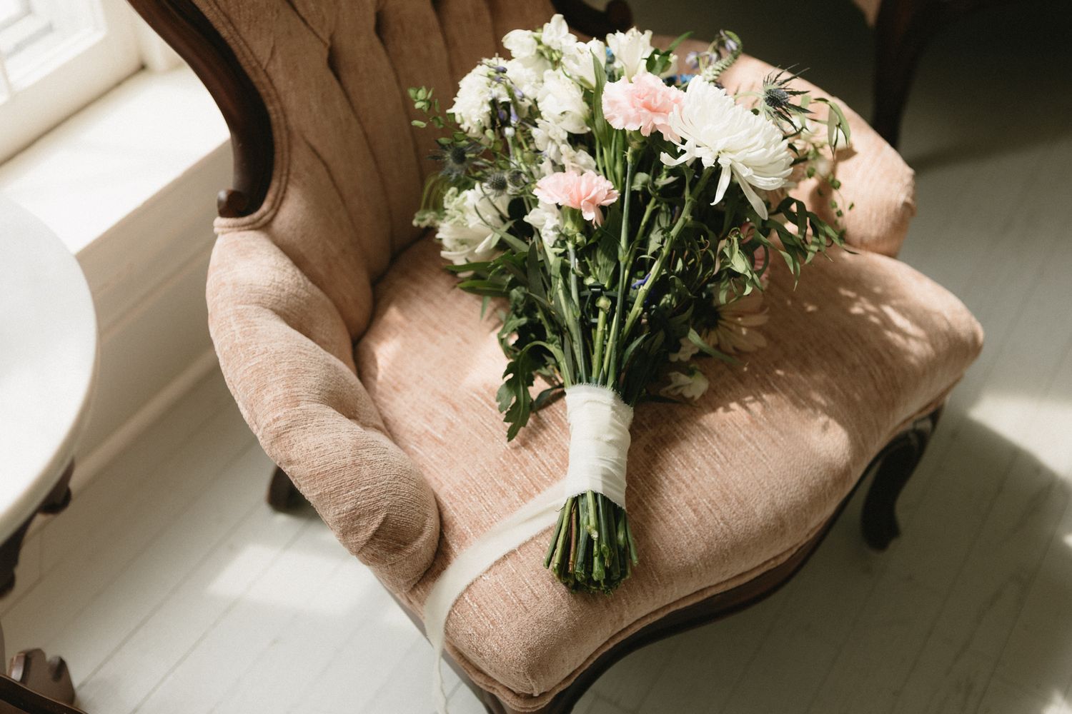 Close-up of elegant bridal shoes with delicate white flowers and soft sunlight streaming in.