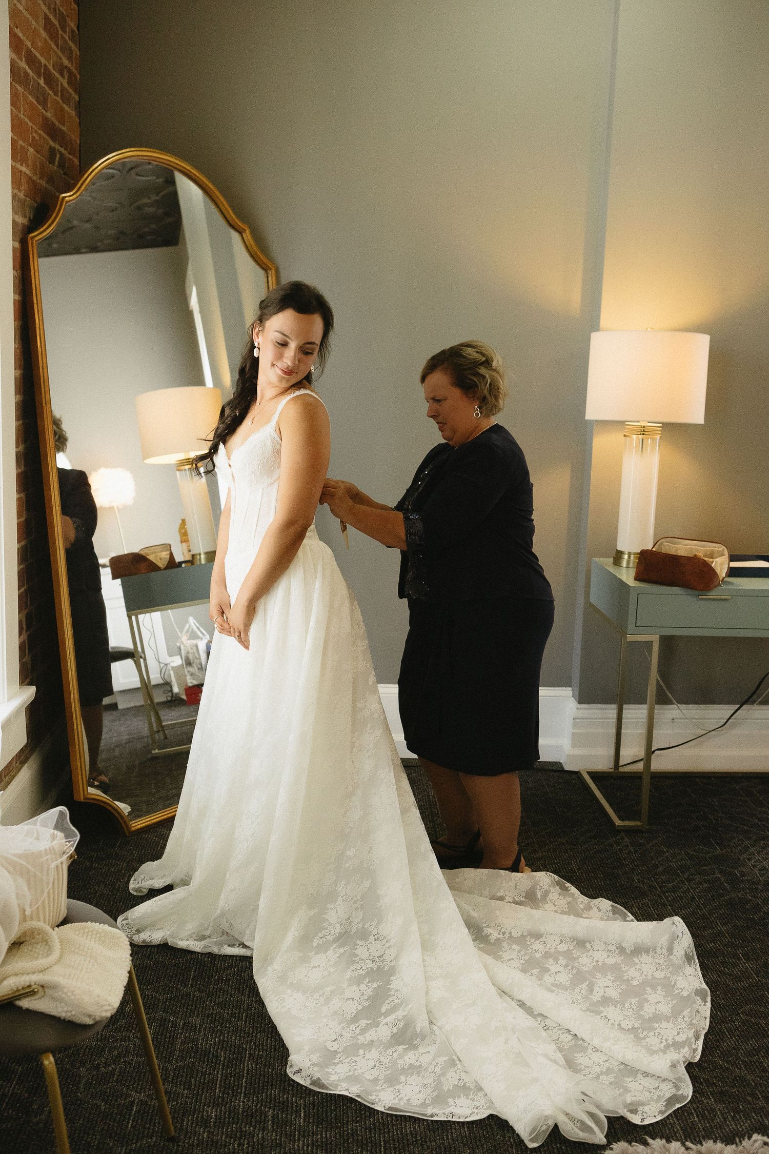 A wedding dress fitting moment showing final adjustments being made to a beautiful lace gown with a long train.