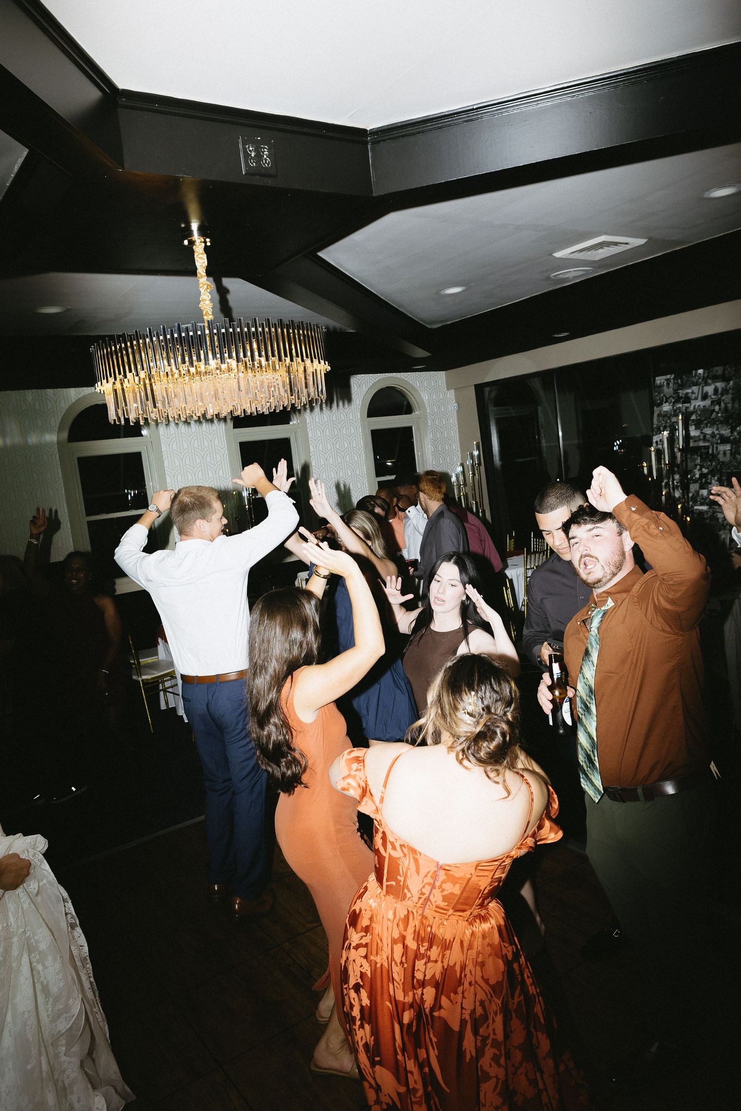 Wedding reception dance floor filled with guests dancing under golden chandelier lighting.