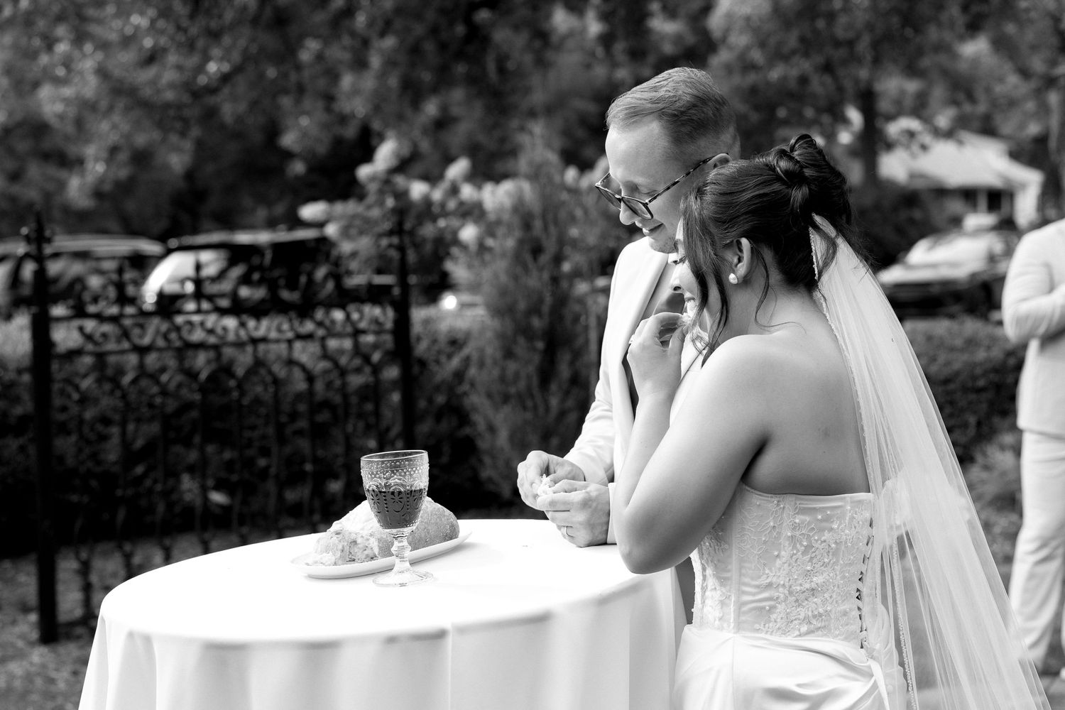 Bride and groom share an intimate moment at white table during outdoor wedding ceremony in black and white.