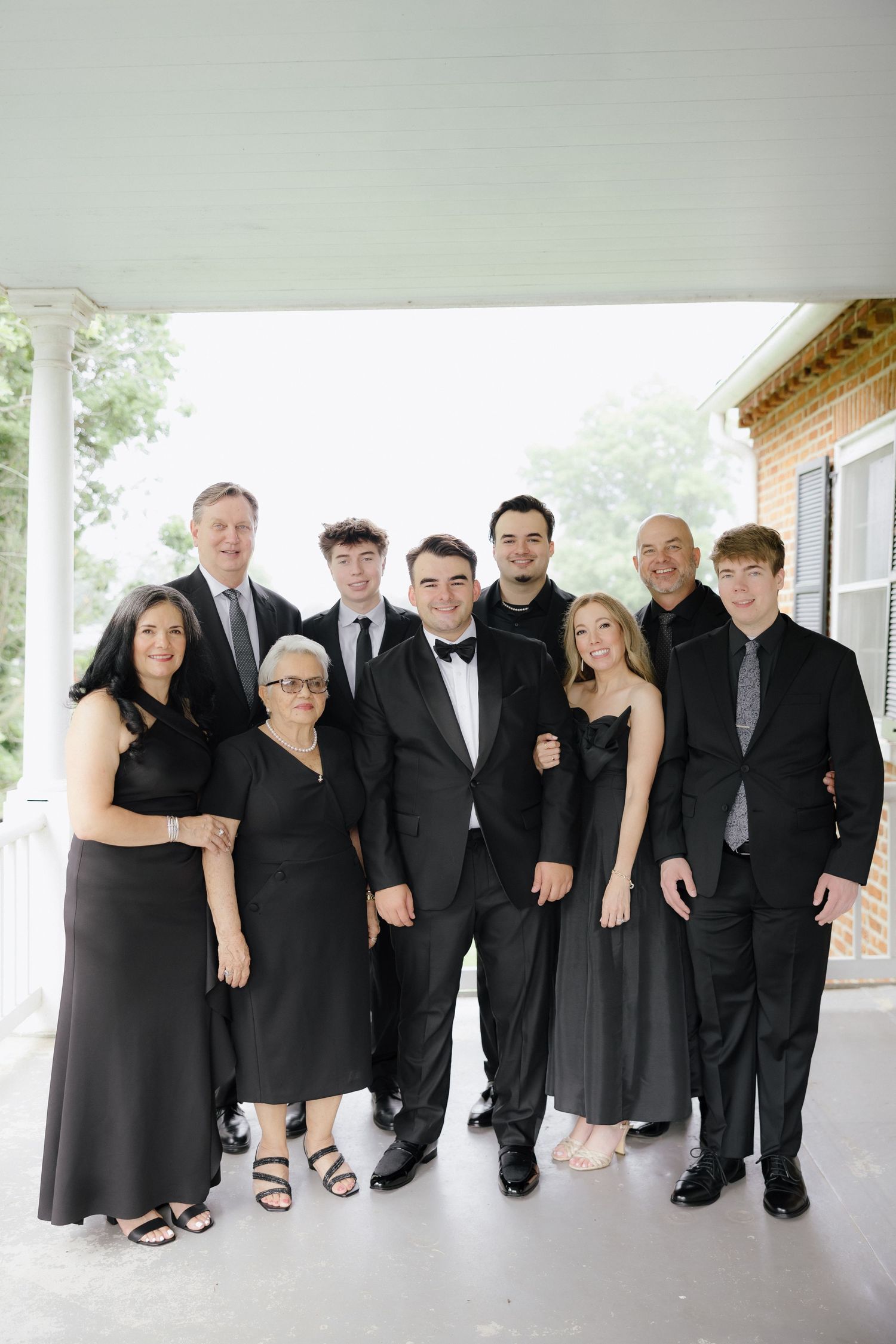 Family group portrait in elegant black formal attire posing together on a porch at a wedding celebration.