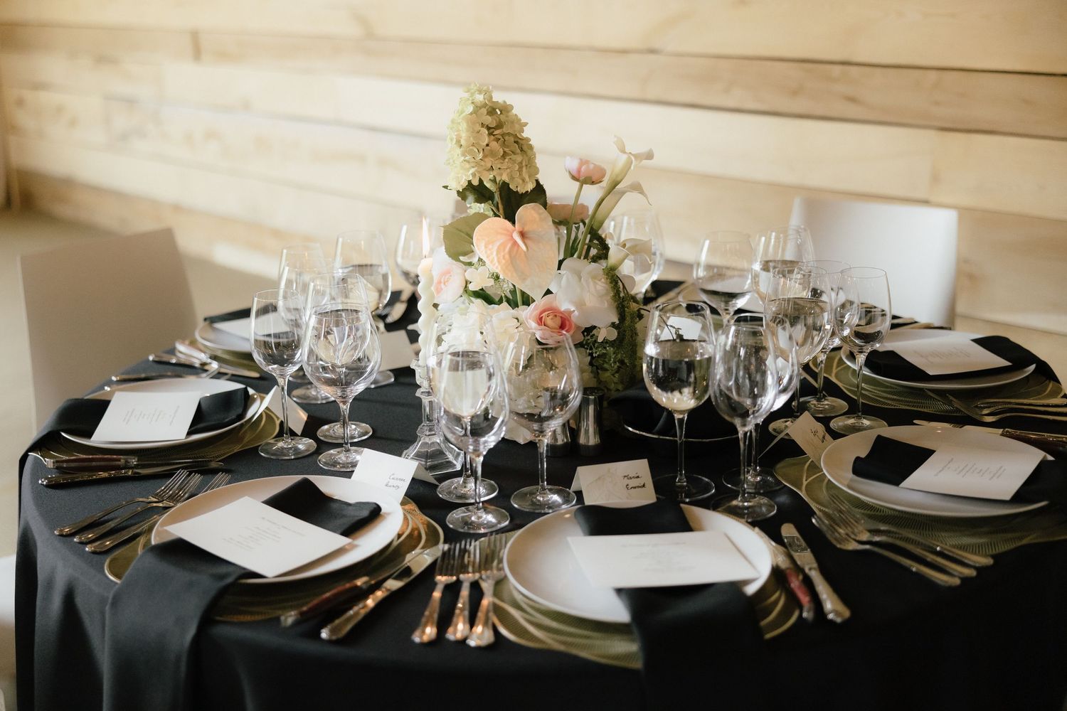 Elegant wedding reception table with black linen, gold chargers, crystal glasses, and pink floral centerpiece.