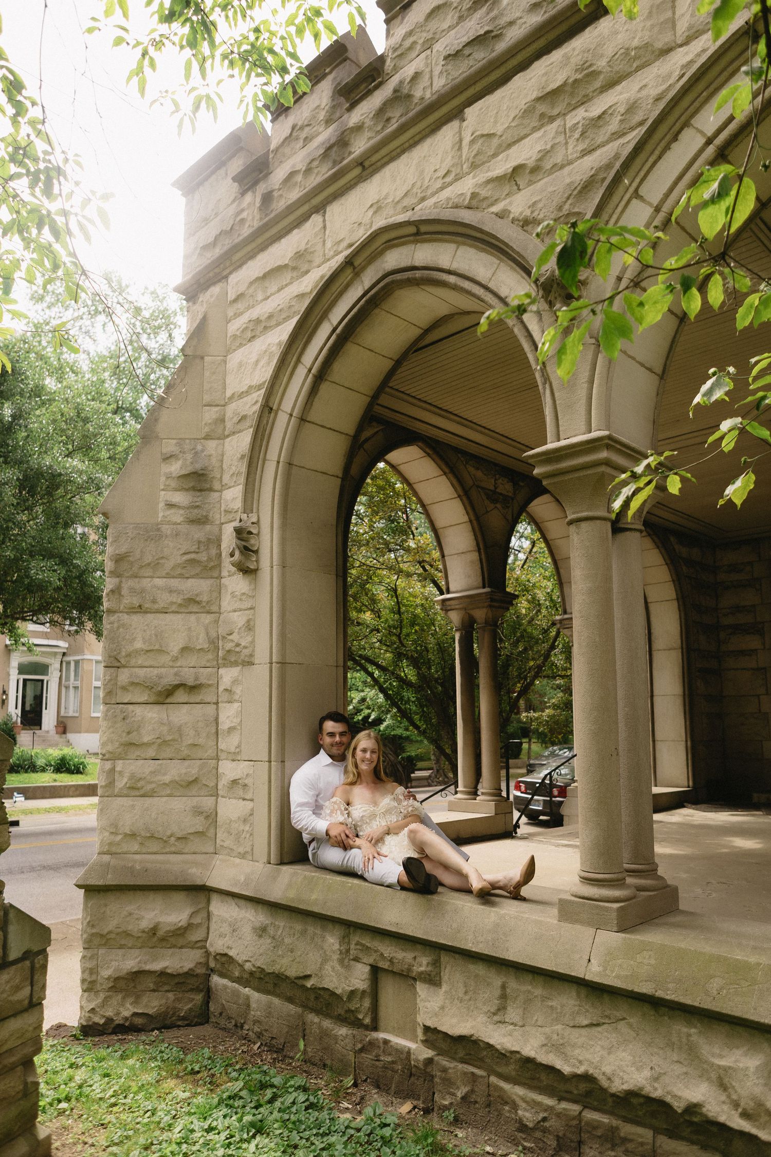 Couple sitting together in a stone archway of a historic building surrounded by lush greenery.