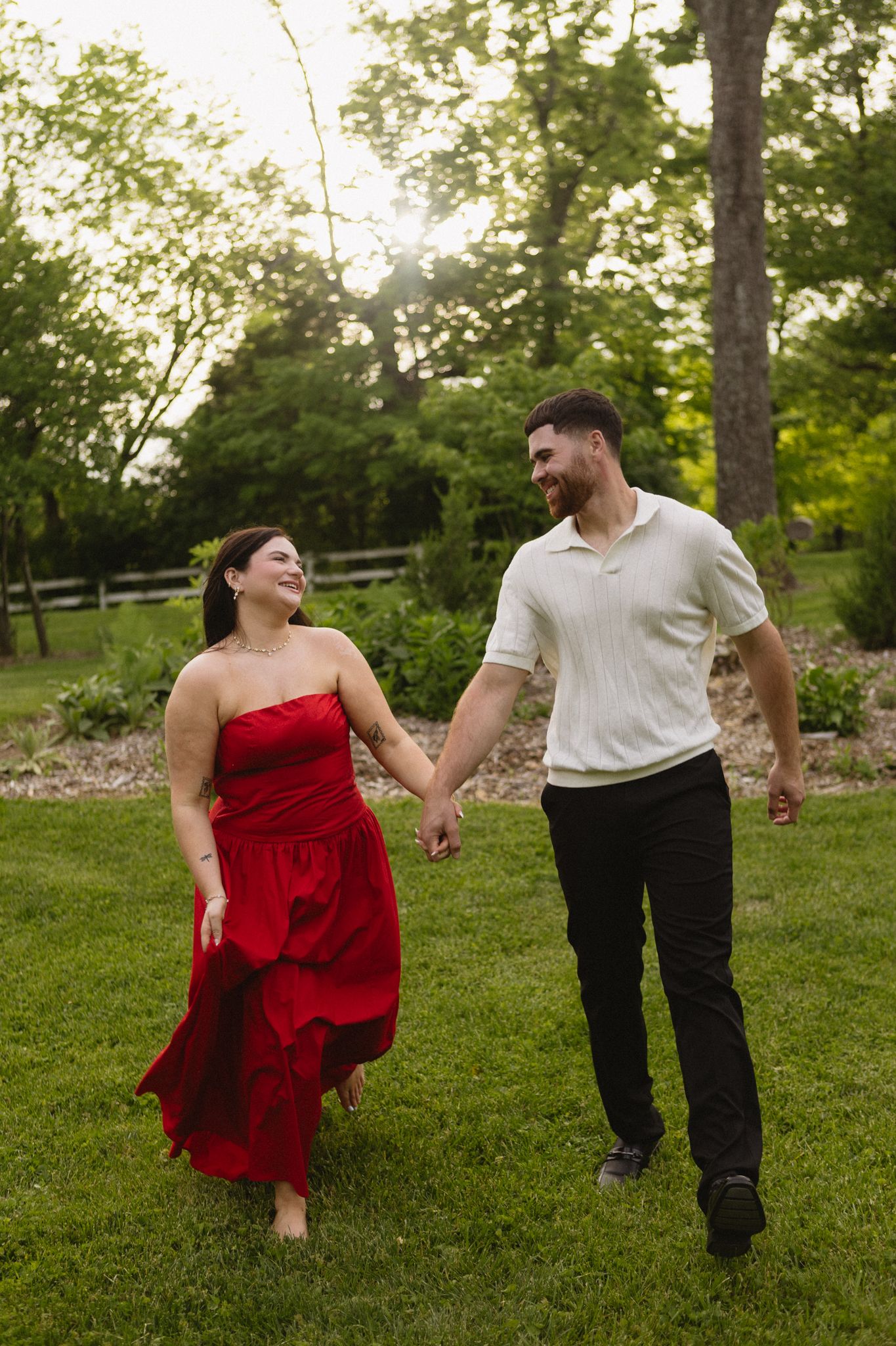 A couple in love dances joyfully together on a lush green lawn with trees in the background.