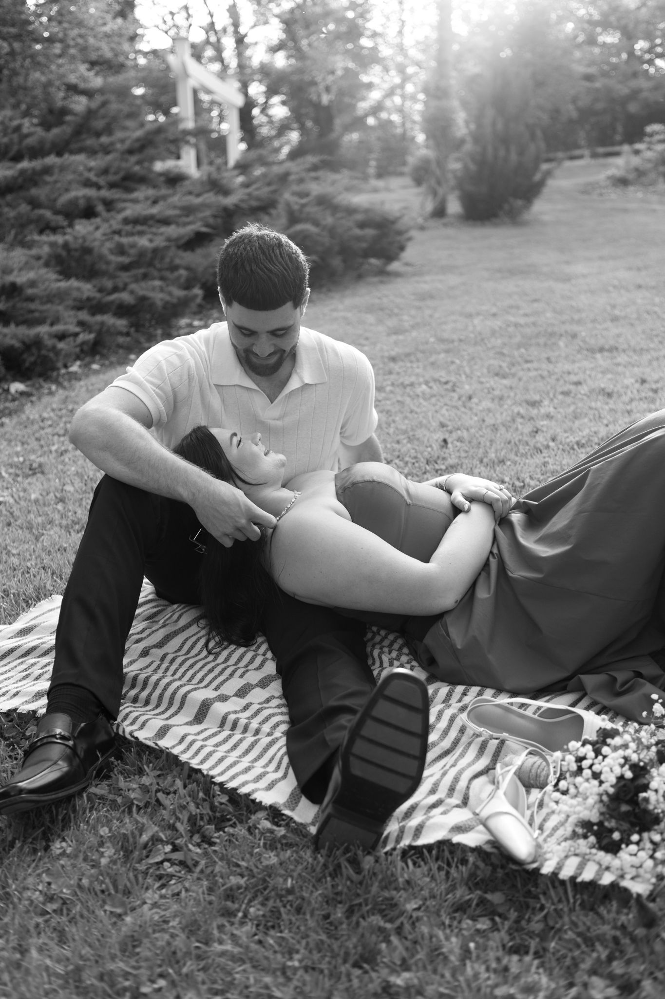 Black and white image of a couple reclining intimately on a blanket in an outdoor garden setting.