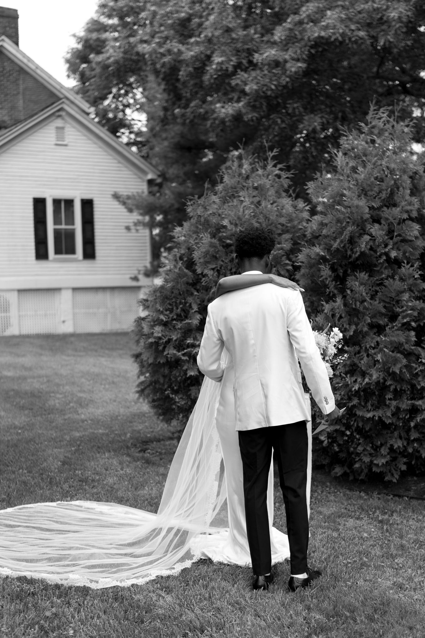 Black and white wedding photos showing the romantic train of a dress trailing across a garden lawn.