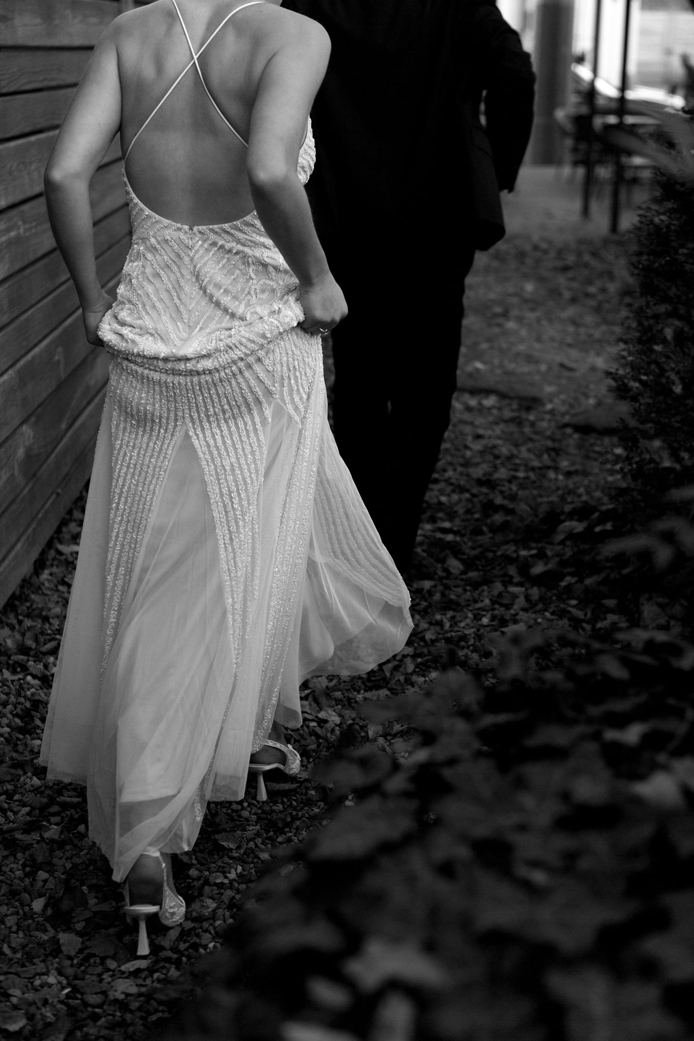 Detailed black and white photo of bride's beaded dress back and silhouette against wooden wall.