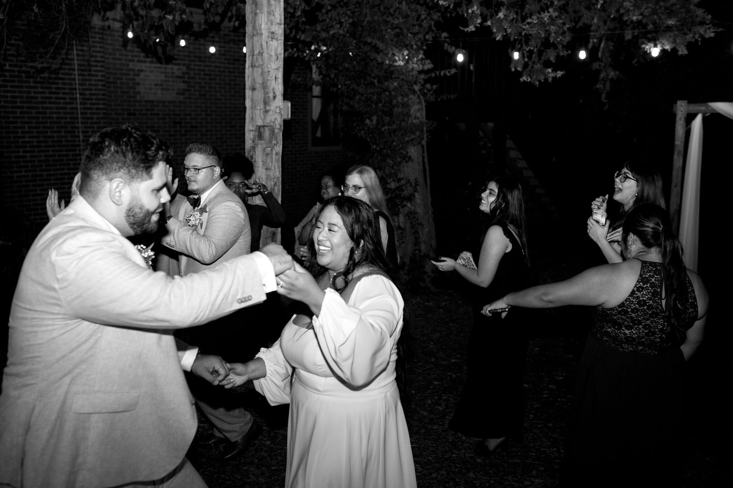 A couple dancing together at a nighttime outdoor party with string lights and other attendees in the background.