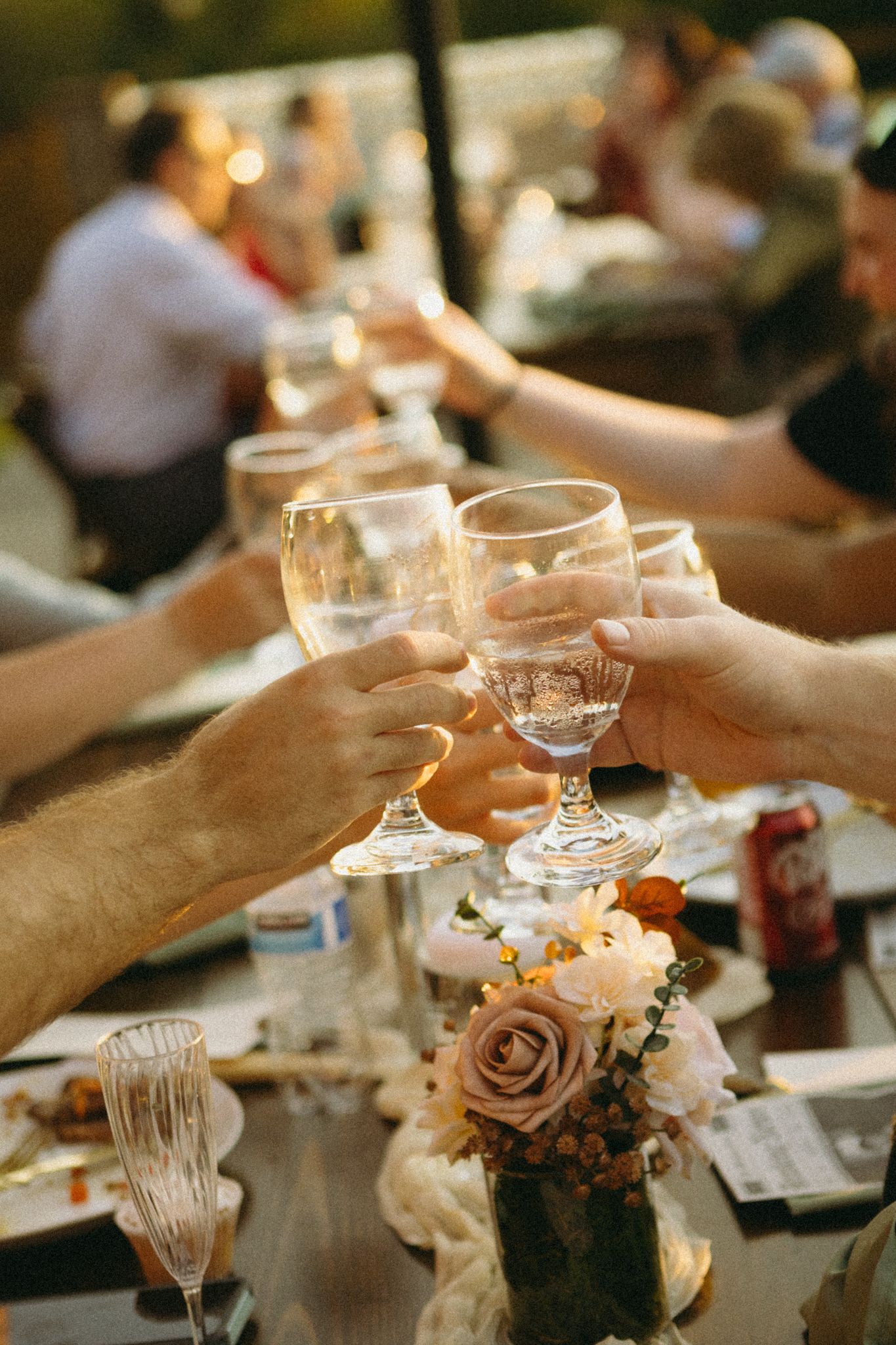 Wedding guests raise glasses in a celebratory toast at a reception table decorated with floral centerpieces.