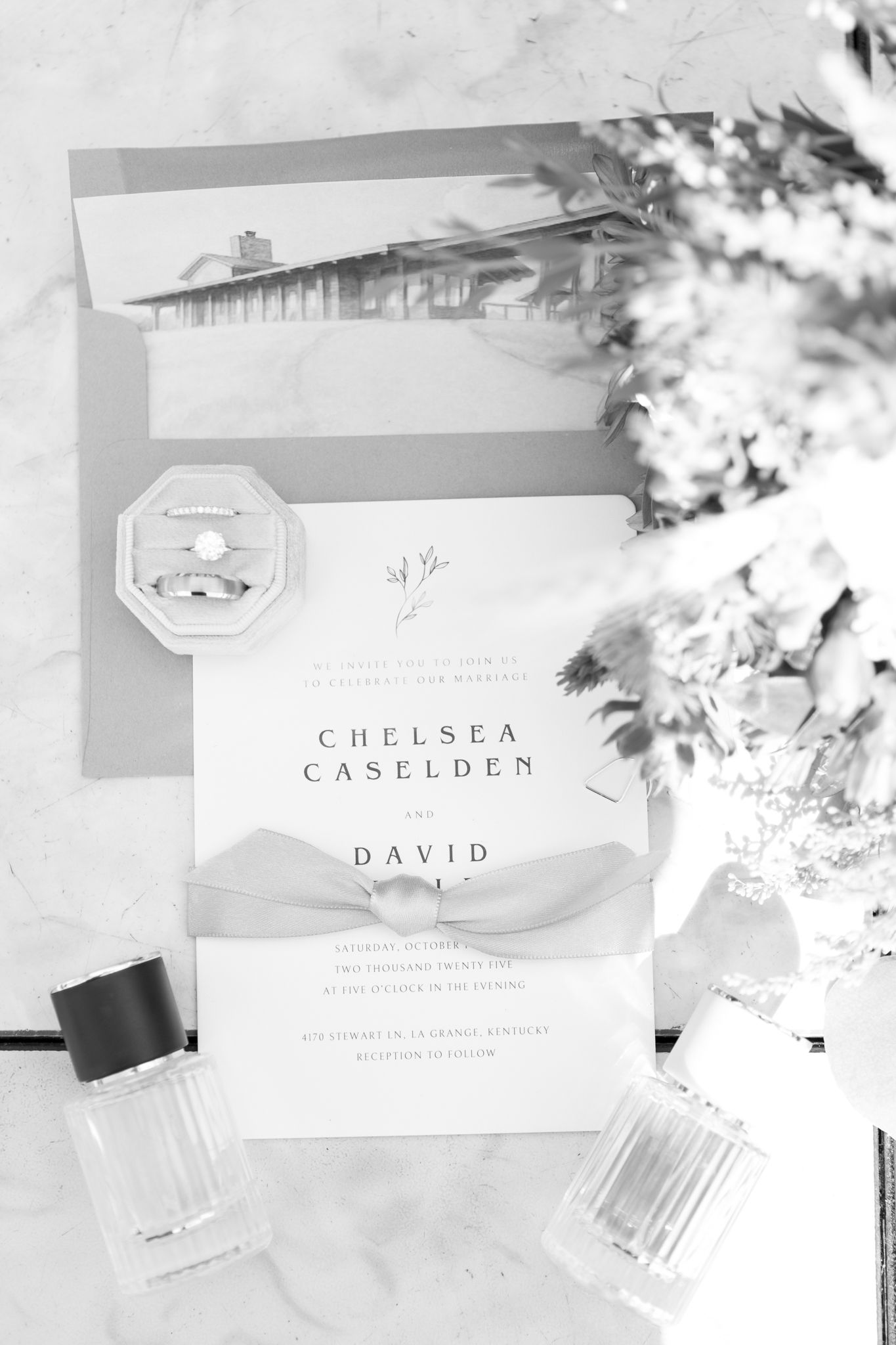 Elegant black and white wedding invitation with floral details and perfume bottles on a light background.