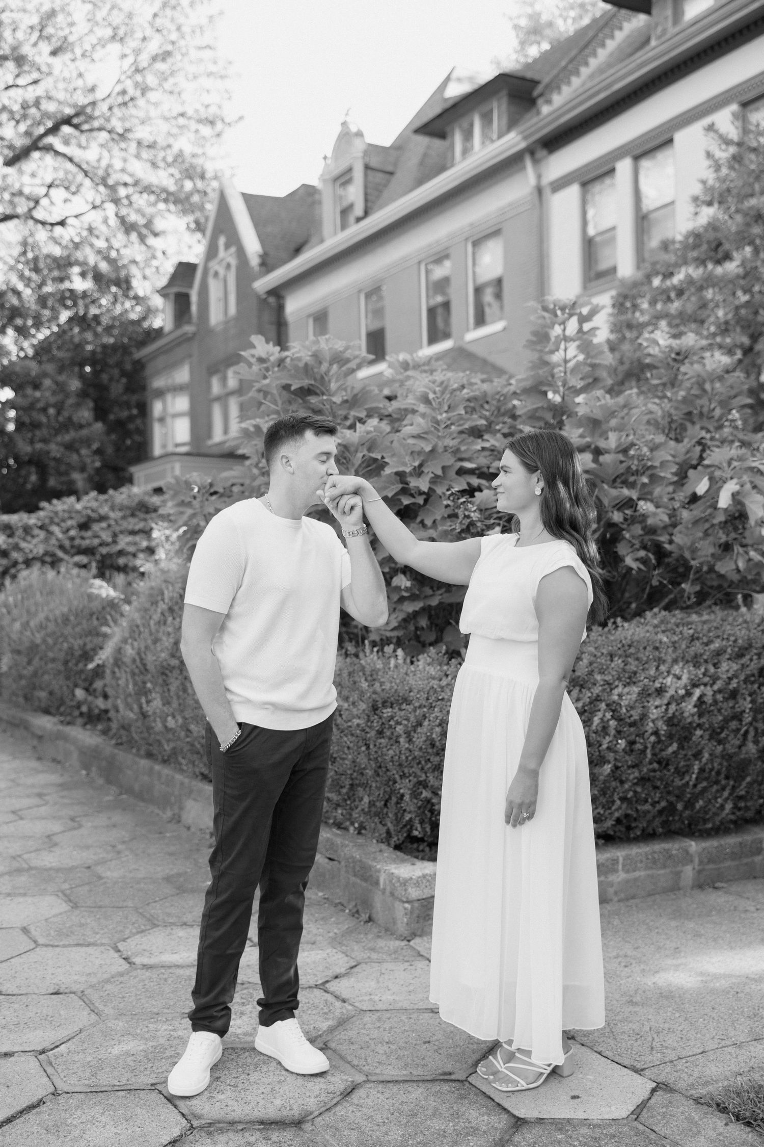 Black and white photo of a man kissing a woman's hand outside a historic brick building.