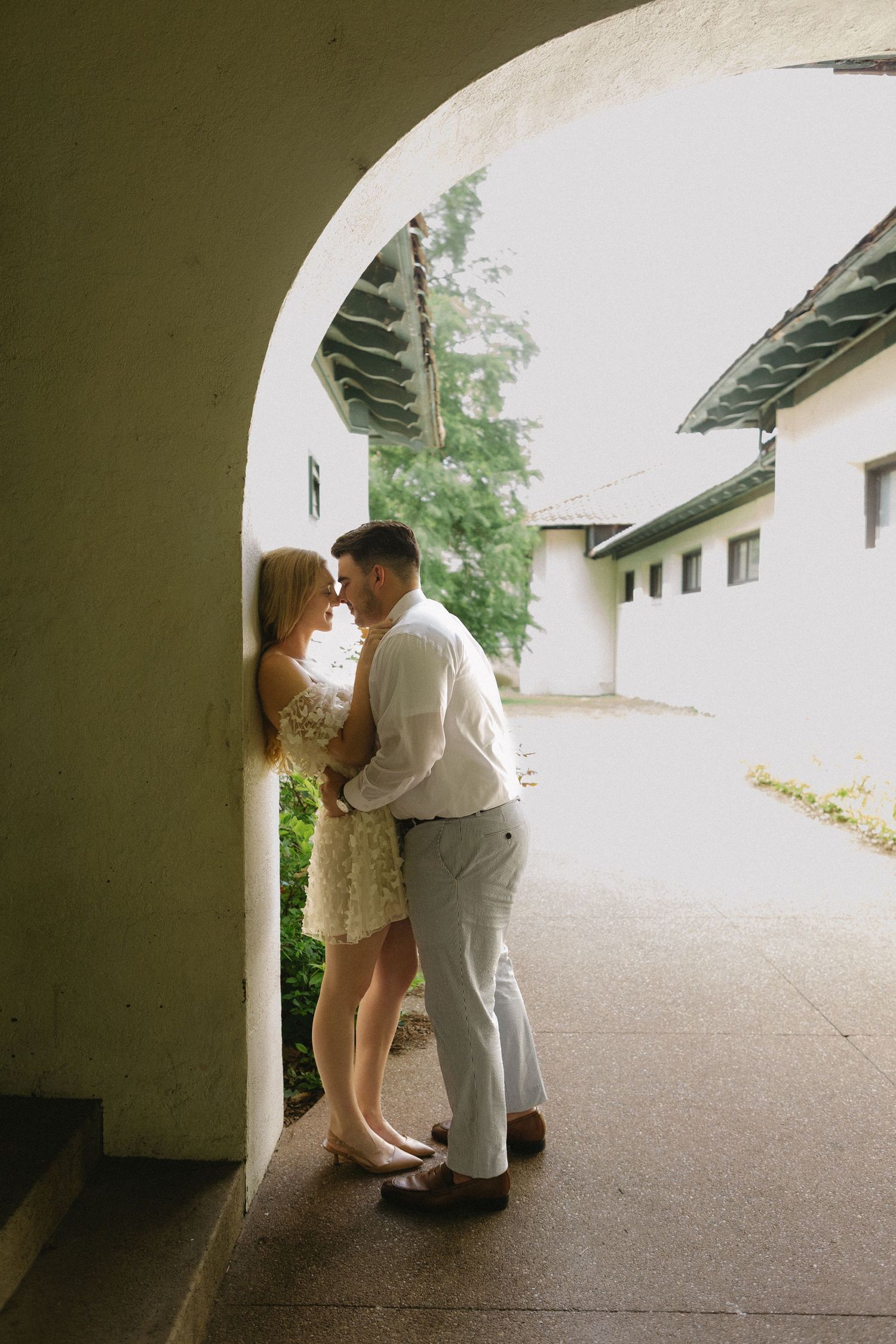 Couple sharing a romantic moment under a stone arch at a historic venue.