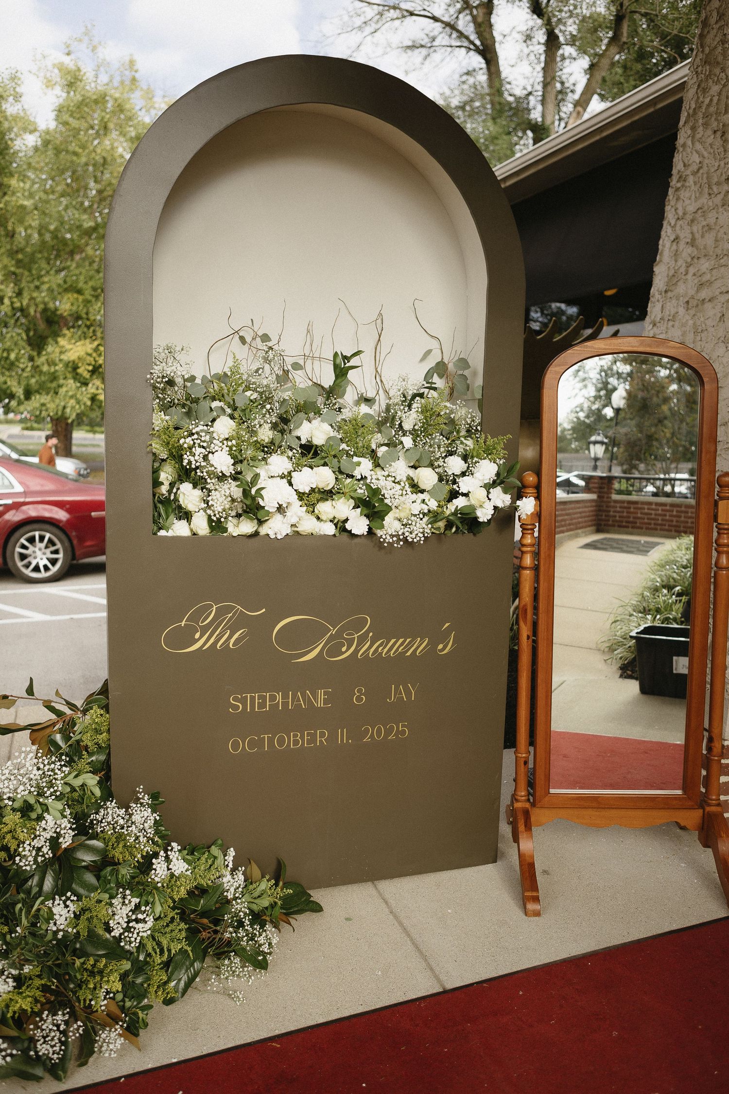 Wedding welcome sign with white floral arrangements and personalized text in an arched frame.