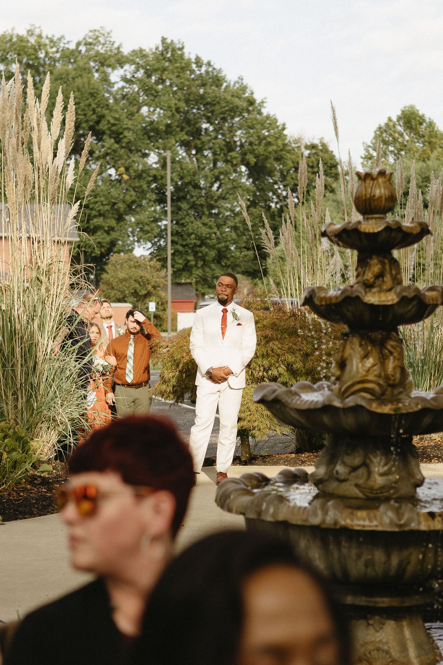 Outdoor wedding scene with ornate fountain and tall grasses in the background.