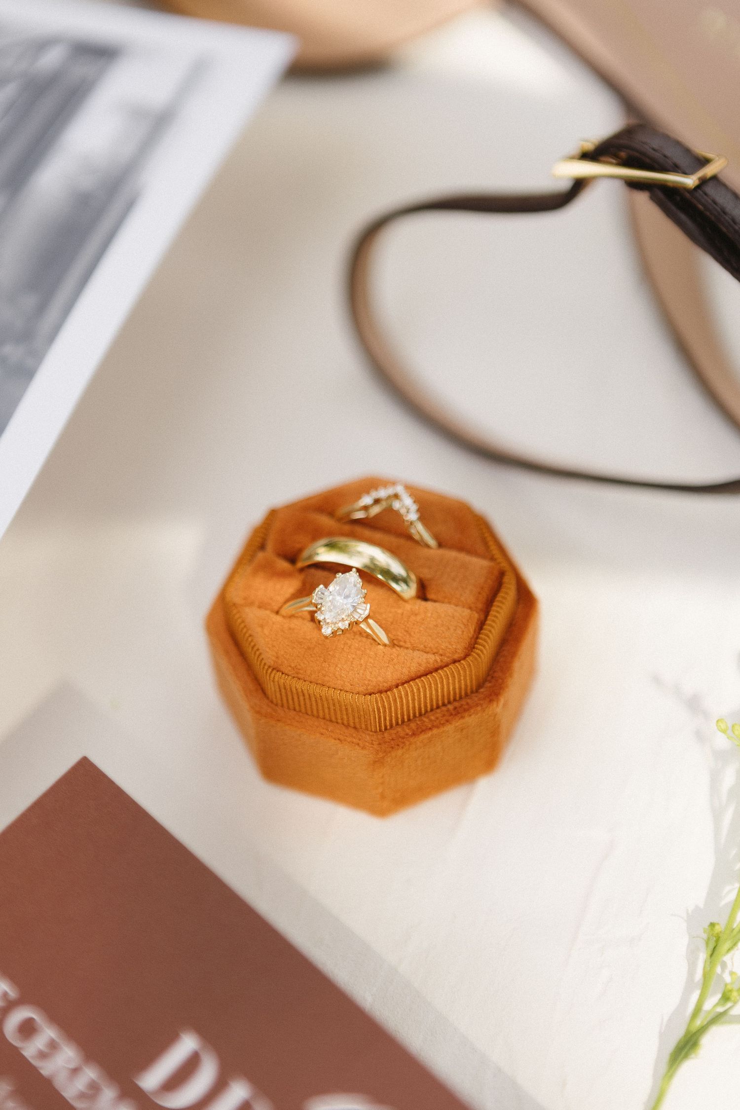 Brown octagonal ring box with gold jewelry displayed on white surface.