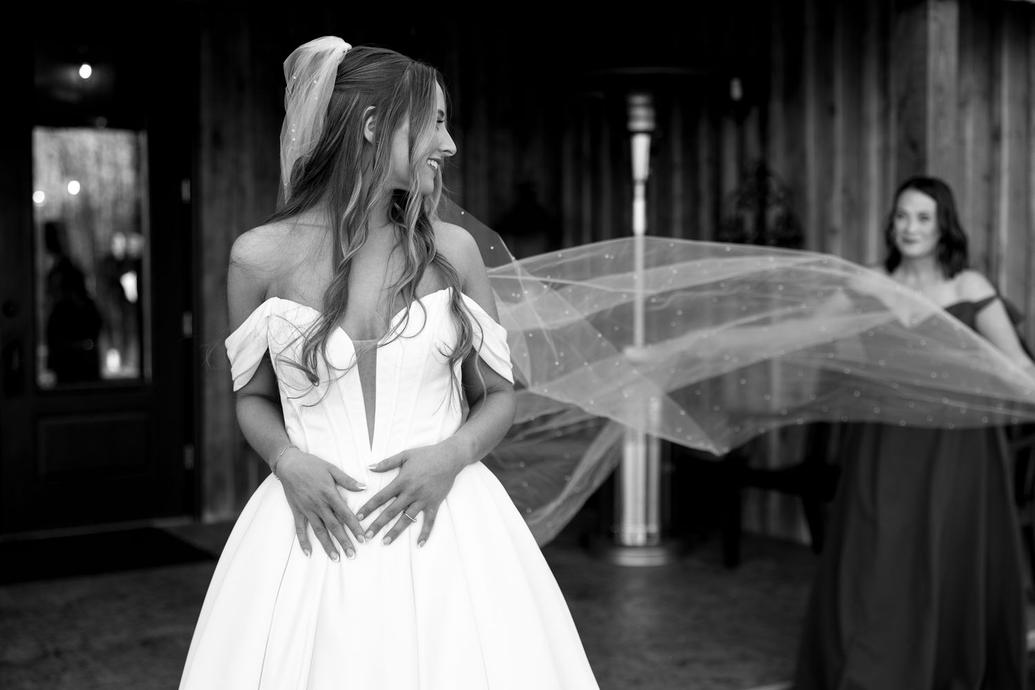 Black and white photo of flowing bridal veil catching wind against wooden background.
