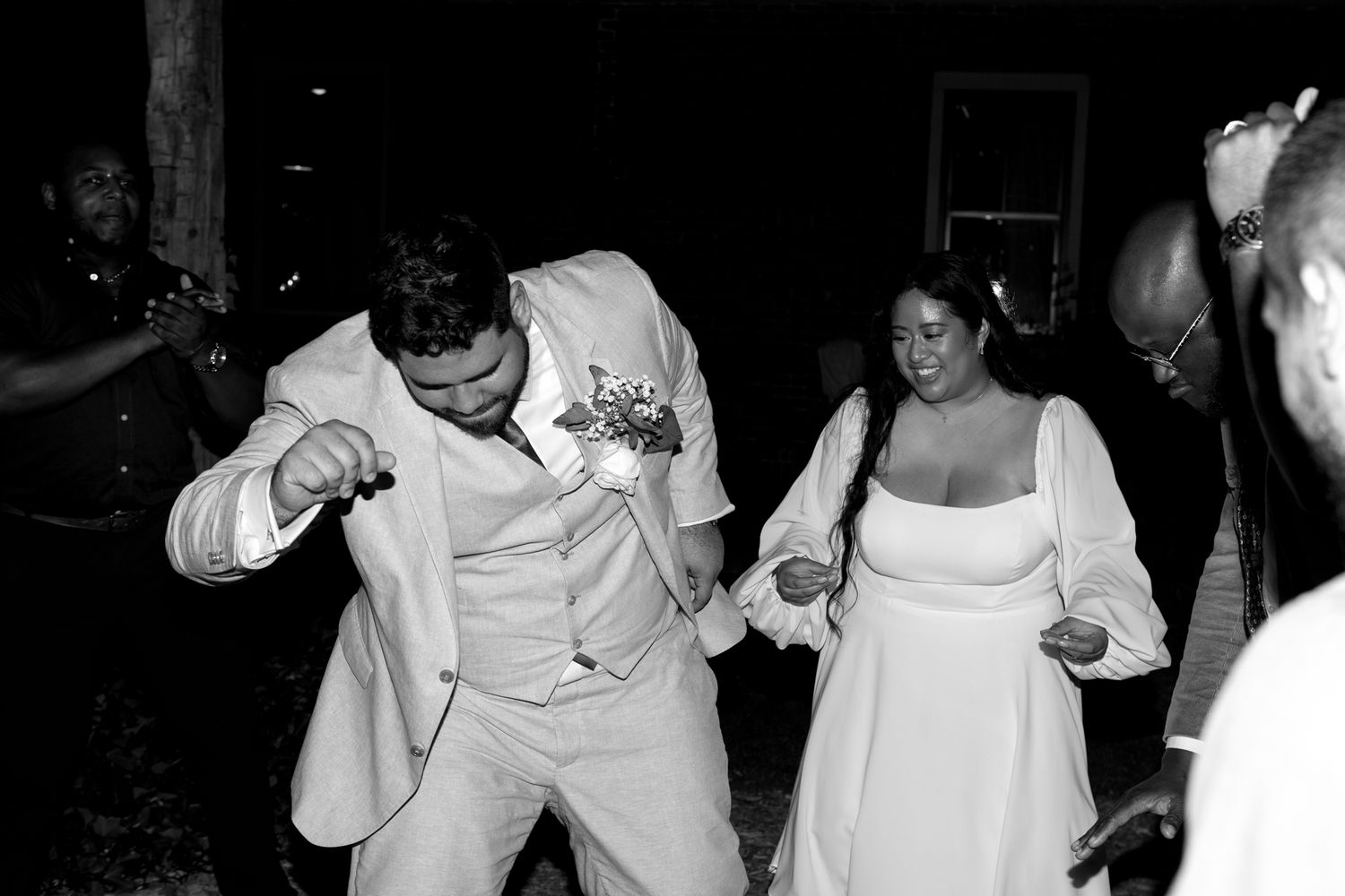 A group of people dancing and celebrating at night under string lights at an outdoor party.