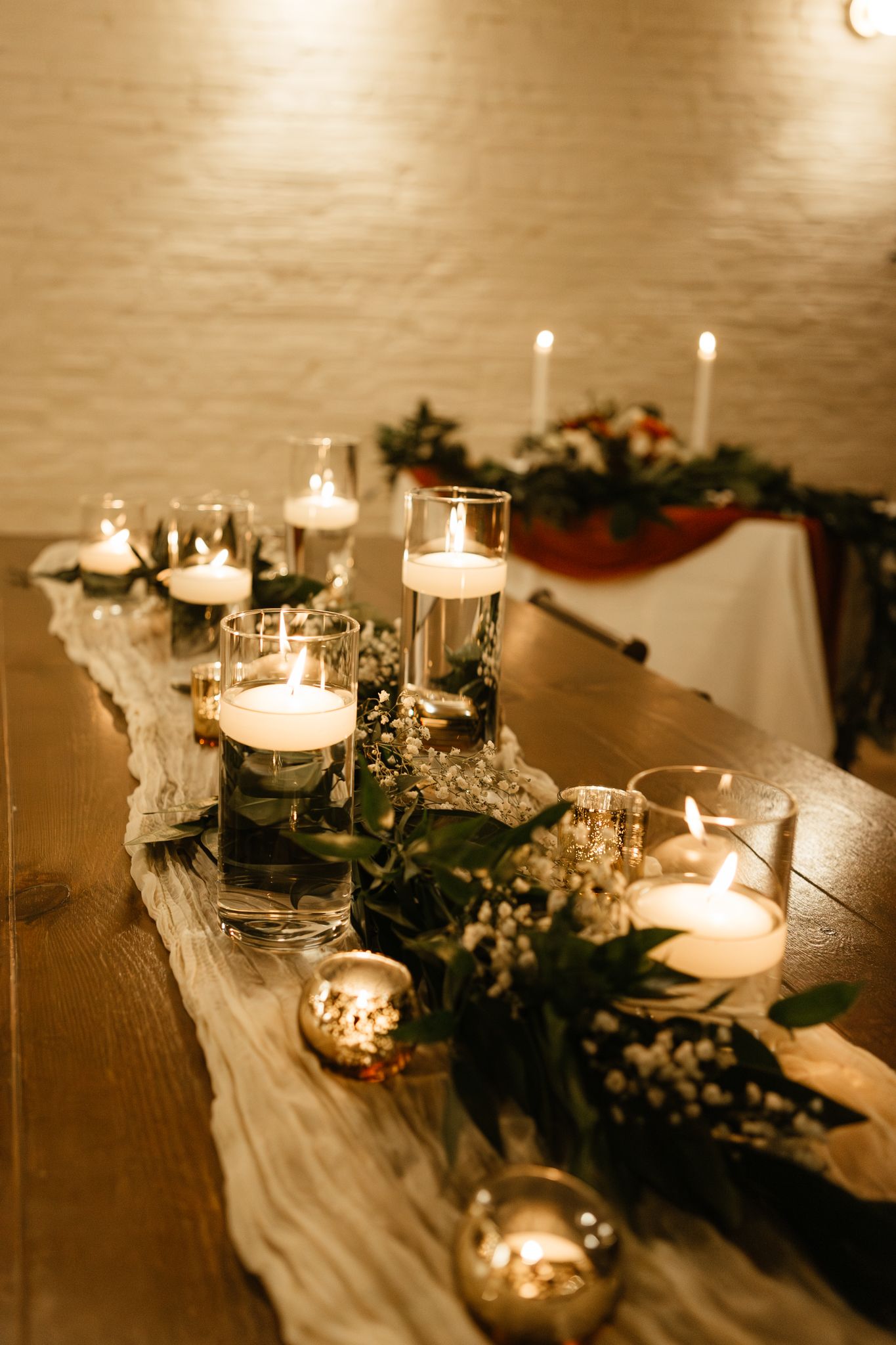 Candlelit table decorated with elegant white fabric runner, greenery, and glowing votives for an intimate event setting.