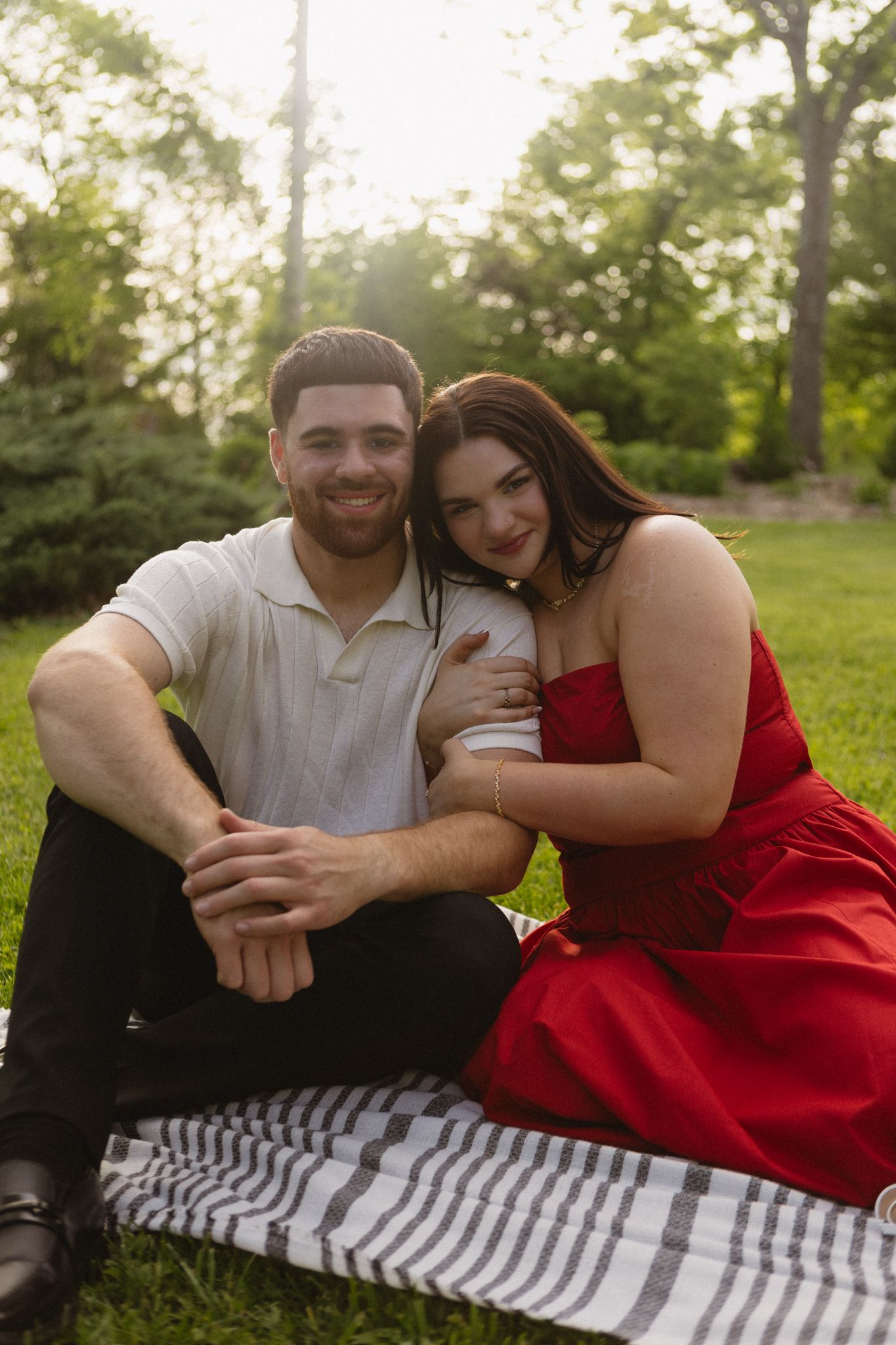 Romantic couple lounging on striped blanket in sunny park setting sharing intimate moments in color photo series.