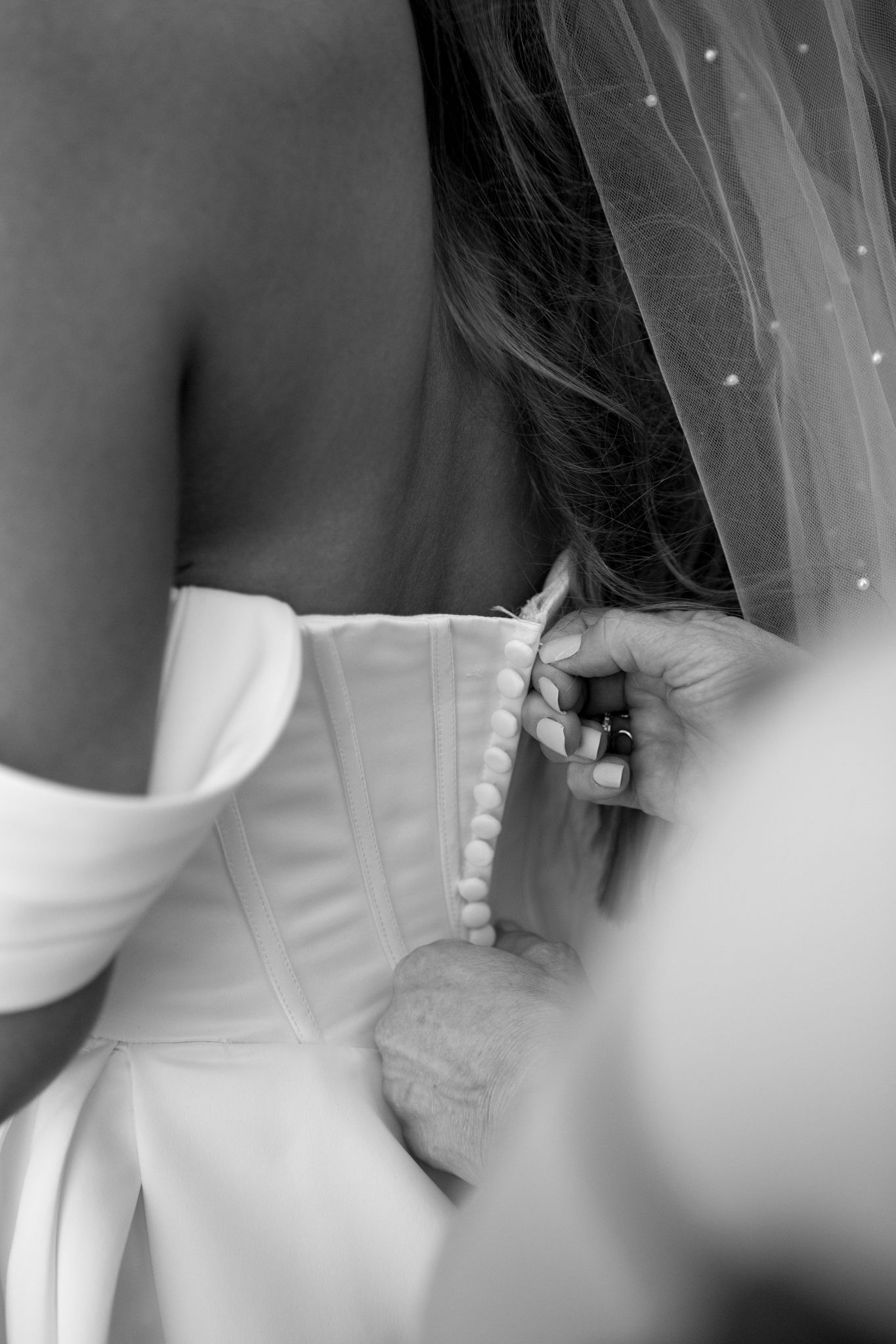 Close-up details of white wedding dress bodice and veil in soft focus.
