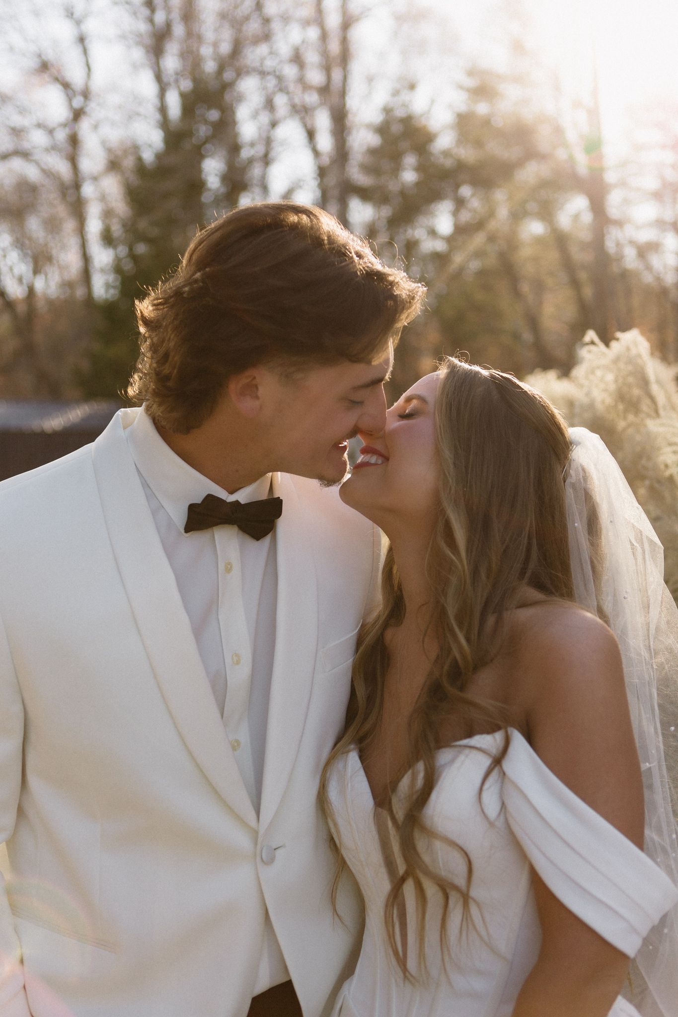 Romantic outdoor wedding portraits of a couple kissing at sunset with glowing natural light.