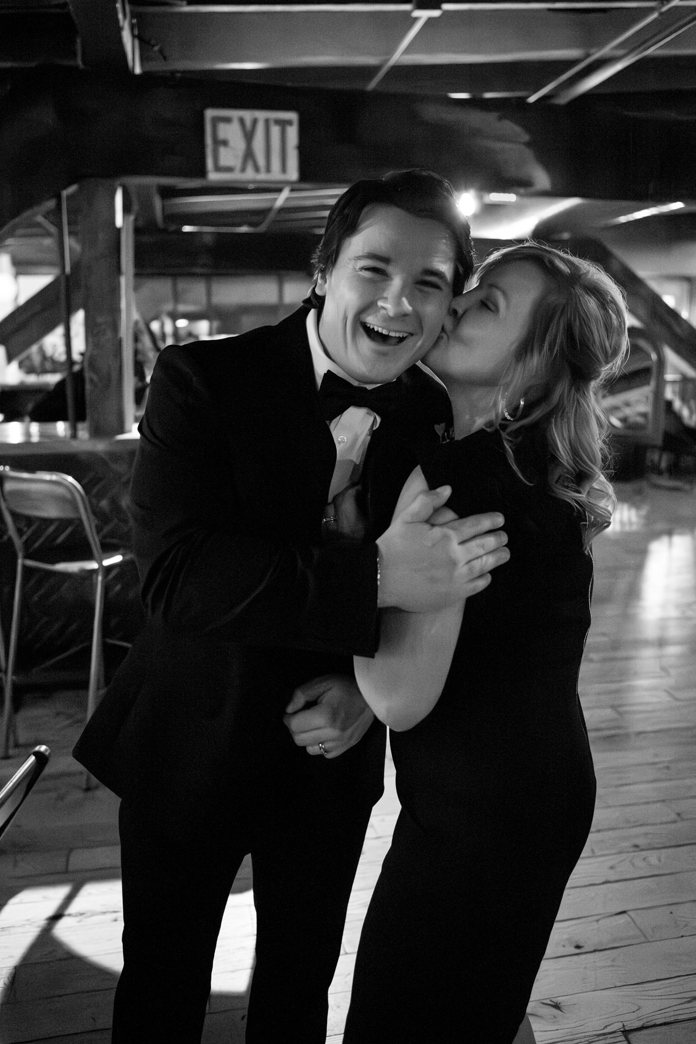 A candid black and white photo showing a loving moment between two people at an indoor venue.