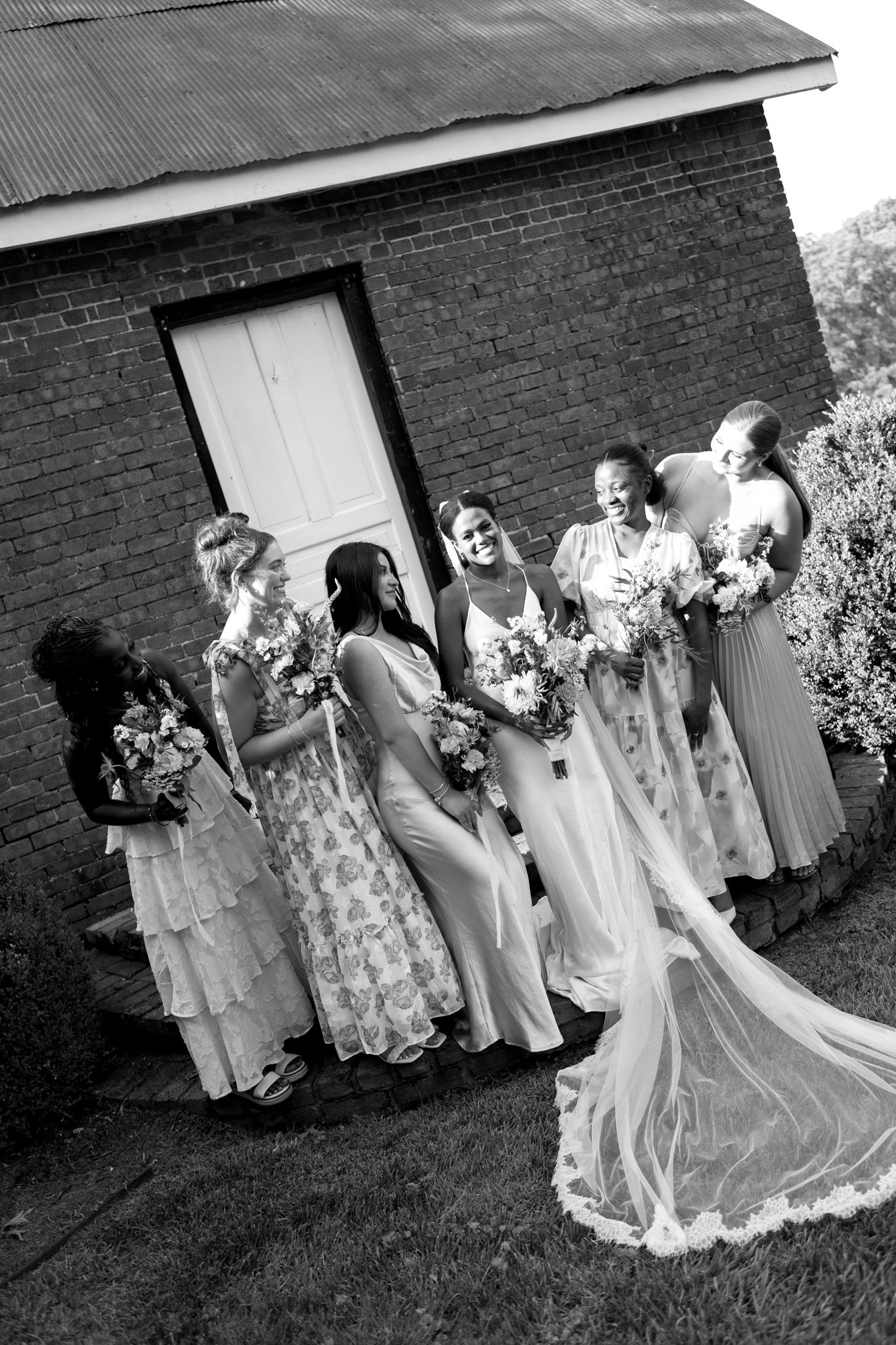 Wedding party poses for formal photos outside a brick building in black and white.