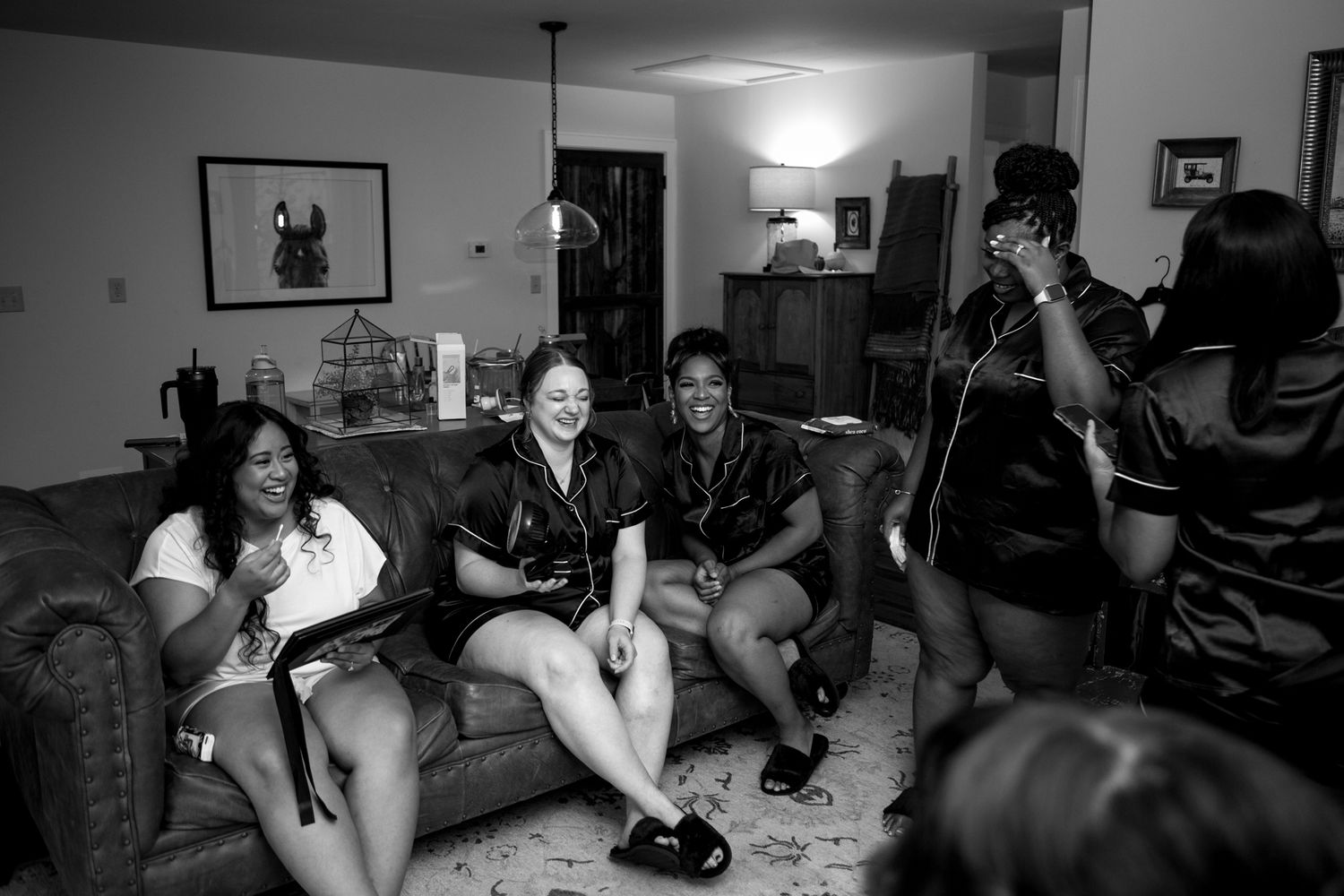 A black and white candid photograph of people laughing together while relaxing on a couch in a living room.