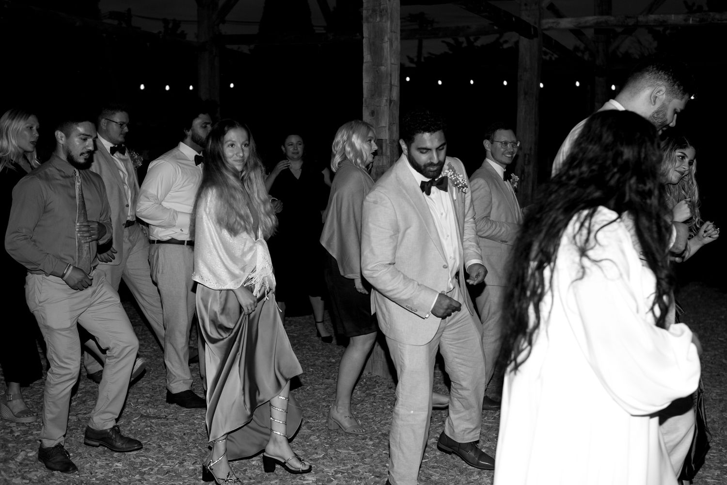 A group of people dancing and celebrating at night under string lights at an outdoor party.