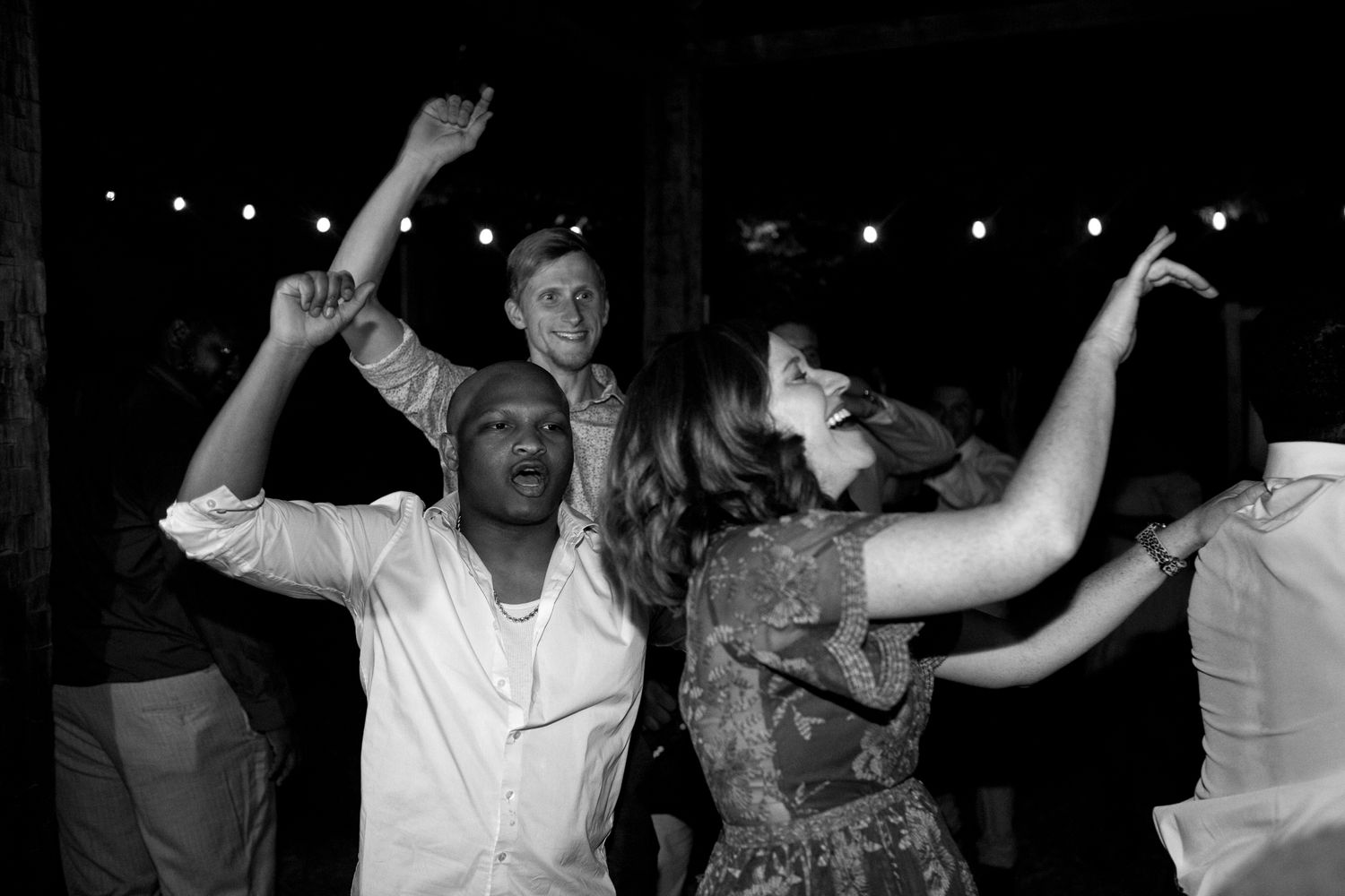 People dancing and celebrating together at a nighttime party with string lights visible in the background.