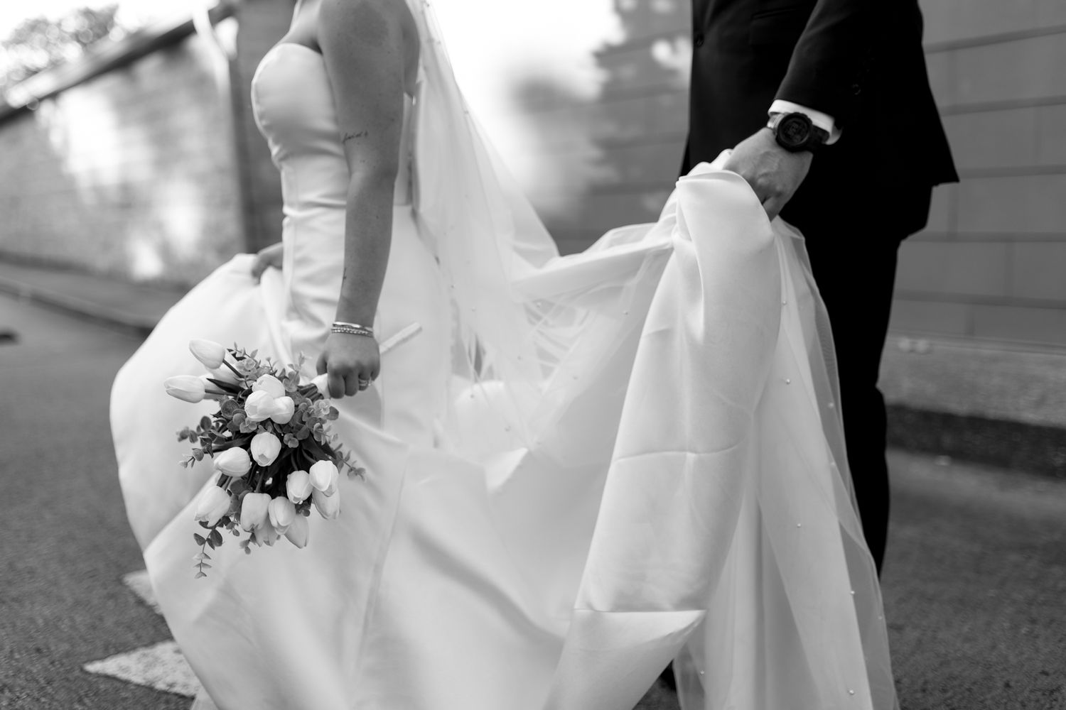 bride and groom walking together, groom helps bride with dress by holding it
