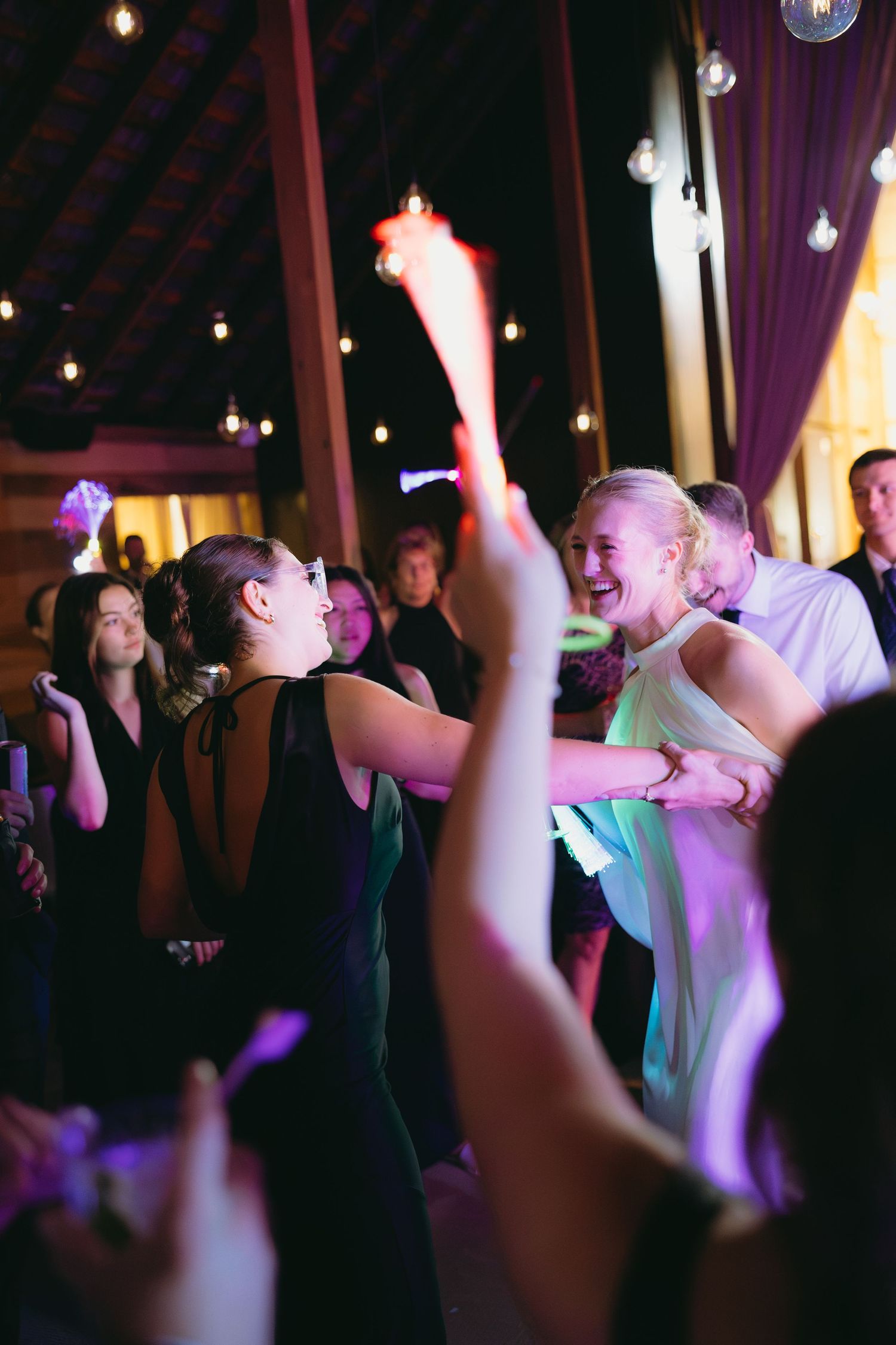 Bride and guests dancing joyfully with glow sticks at lively evening wedding reception.
