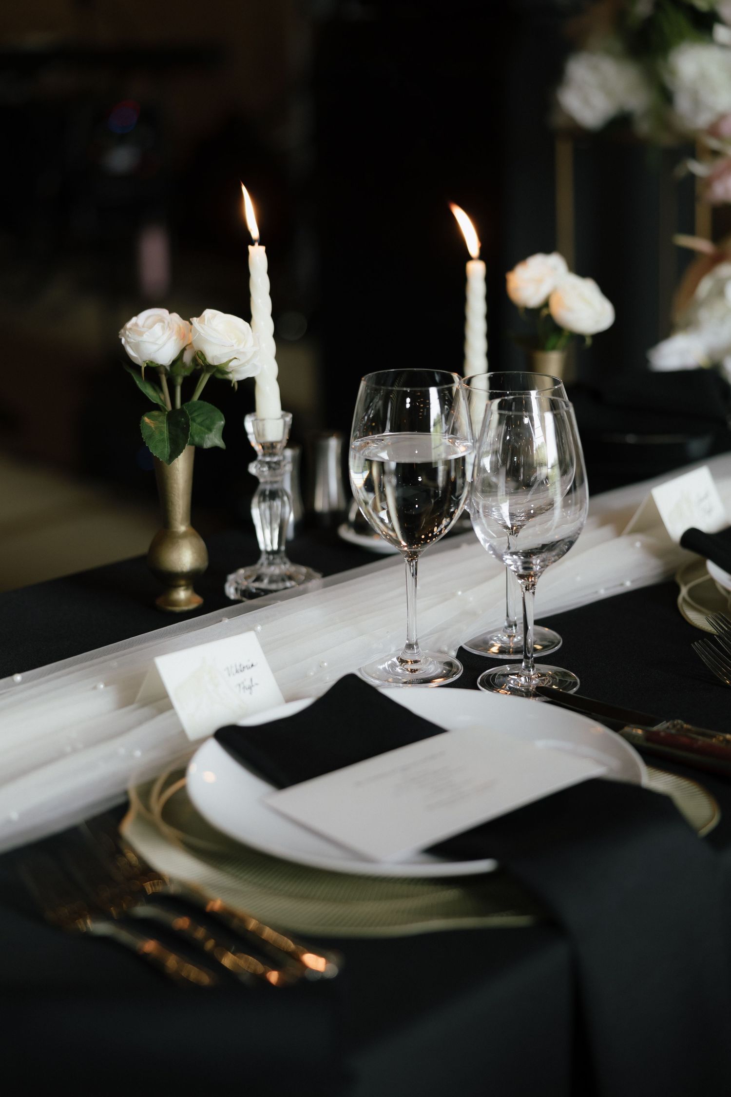 Elegant black and white wedding reception table setting with candles, wine glasses, and white roses.