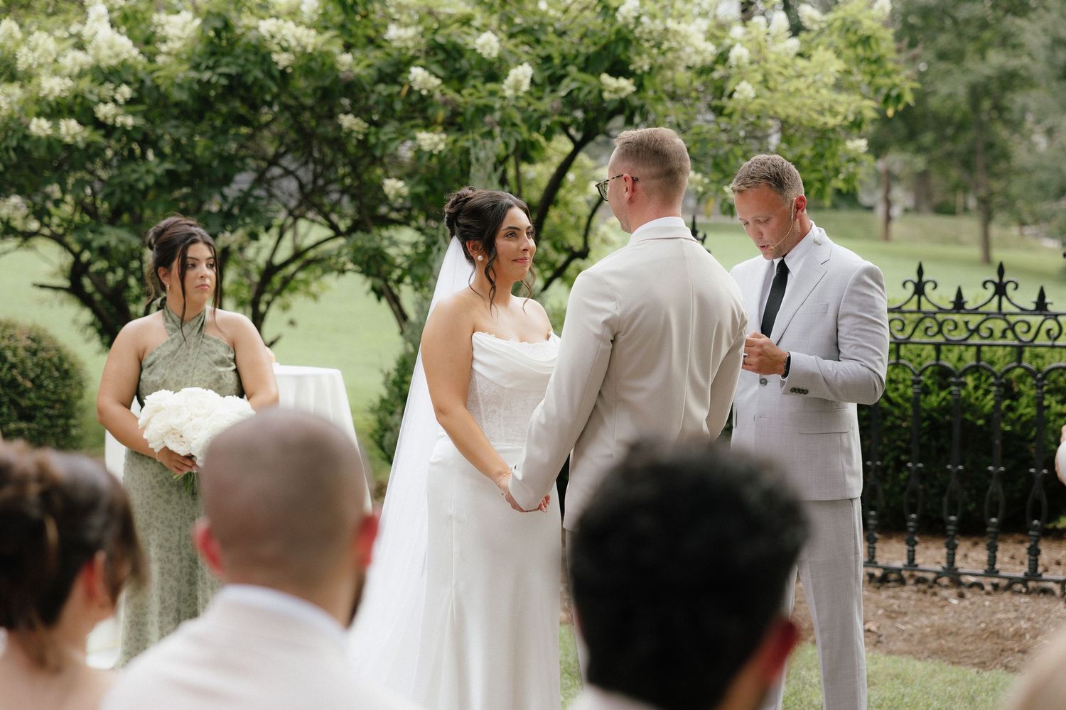 Bride and groom exchanging vows at outdoor garden wedding ceremony with wedding party and guests.