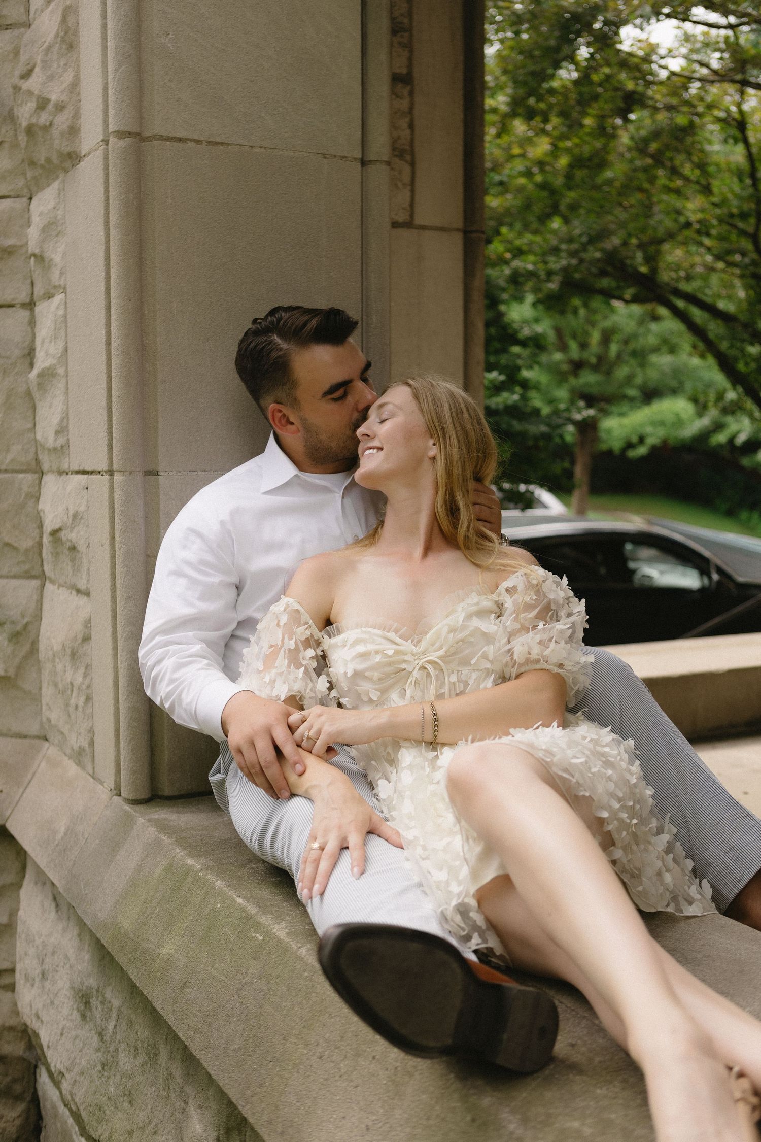 Couple sitting intimately on stone steps of a classic building outdoors.