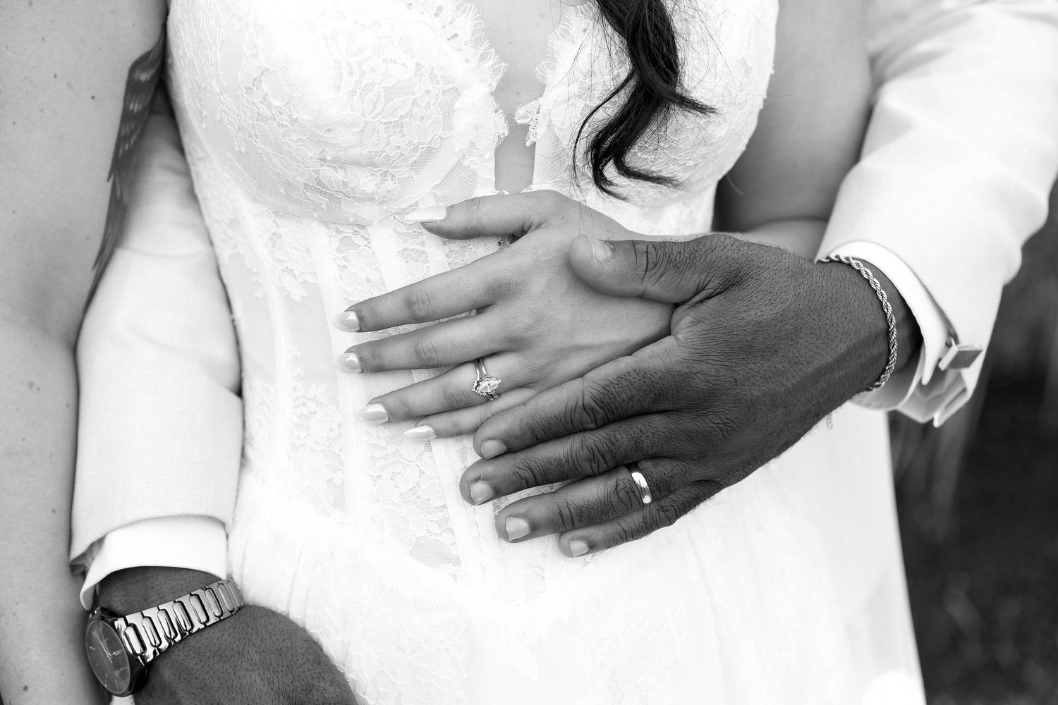 Close-up details of hands and wedding rings against white dress fabric.