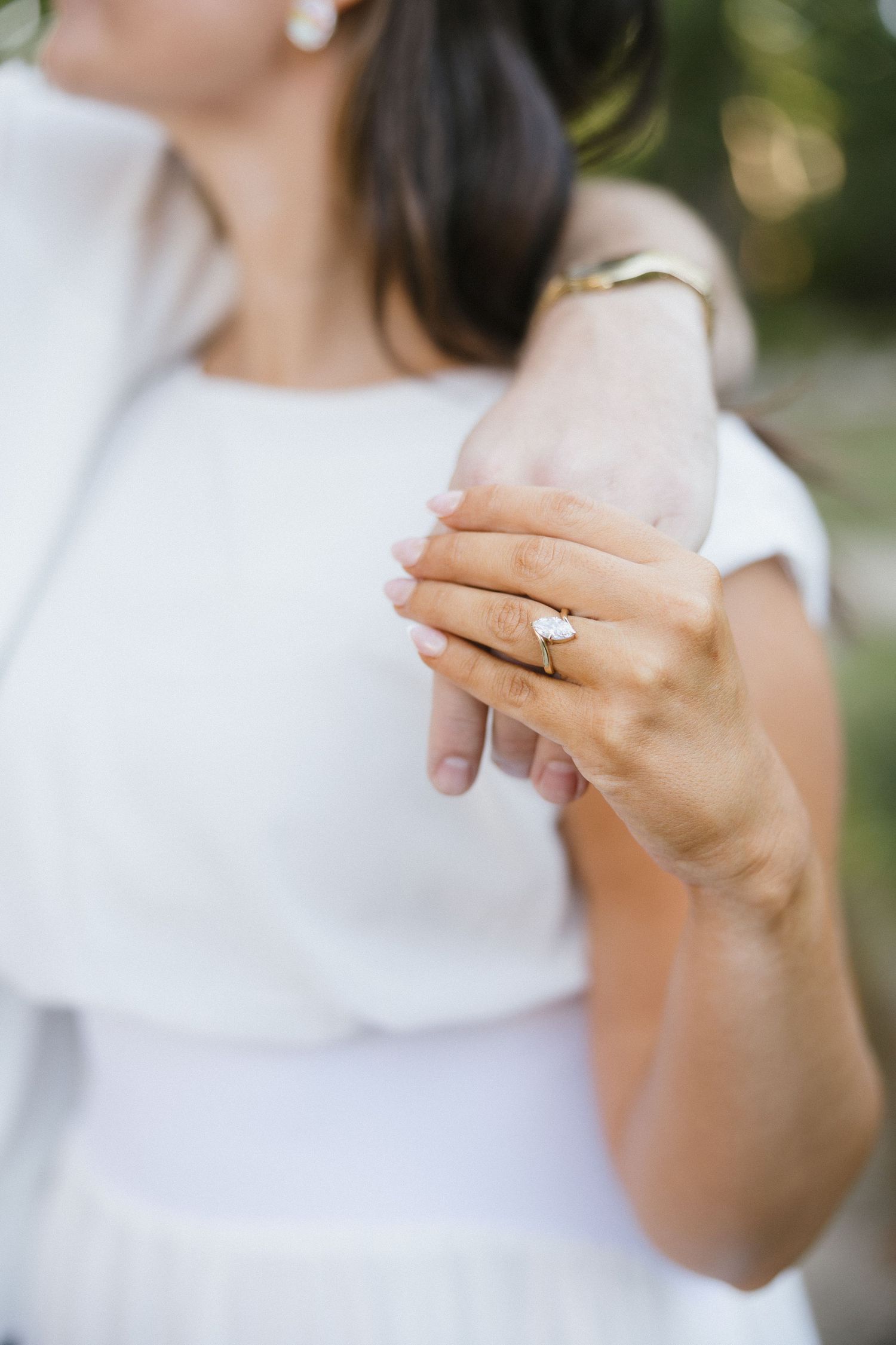 Close-up of a bride in white dress showcasing a diamond engagement ring on her finger.