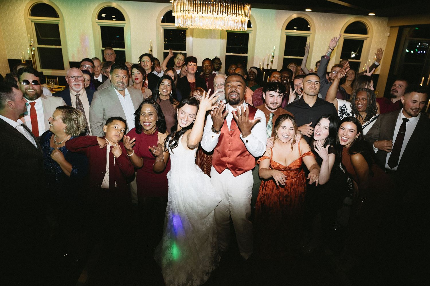 Large group of wedding guests dancing and celebrating at an evening reception.