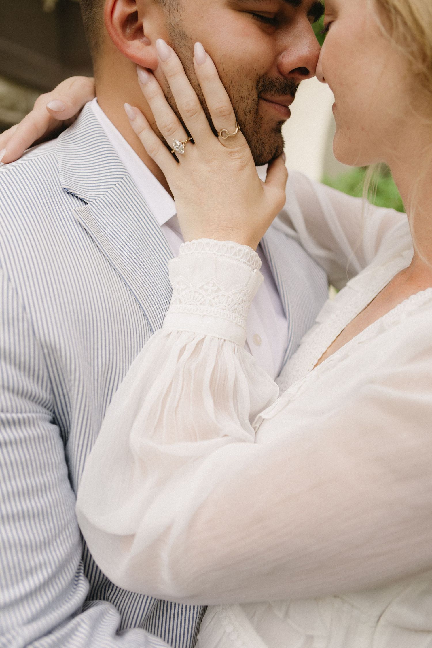 Couple sharing a kiss, bride's hand with gold engagement ring gently cupping groom's face.