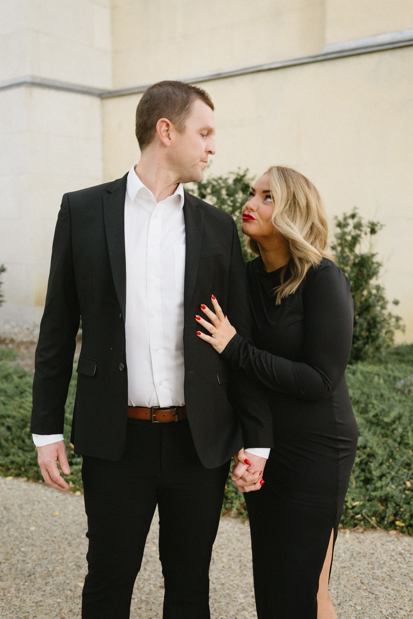 A couple in matching black formal attire share an intimate moment while standing together outdoors.