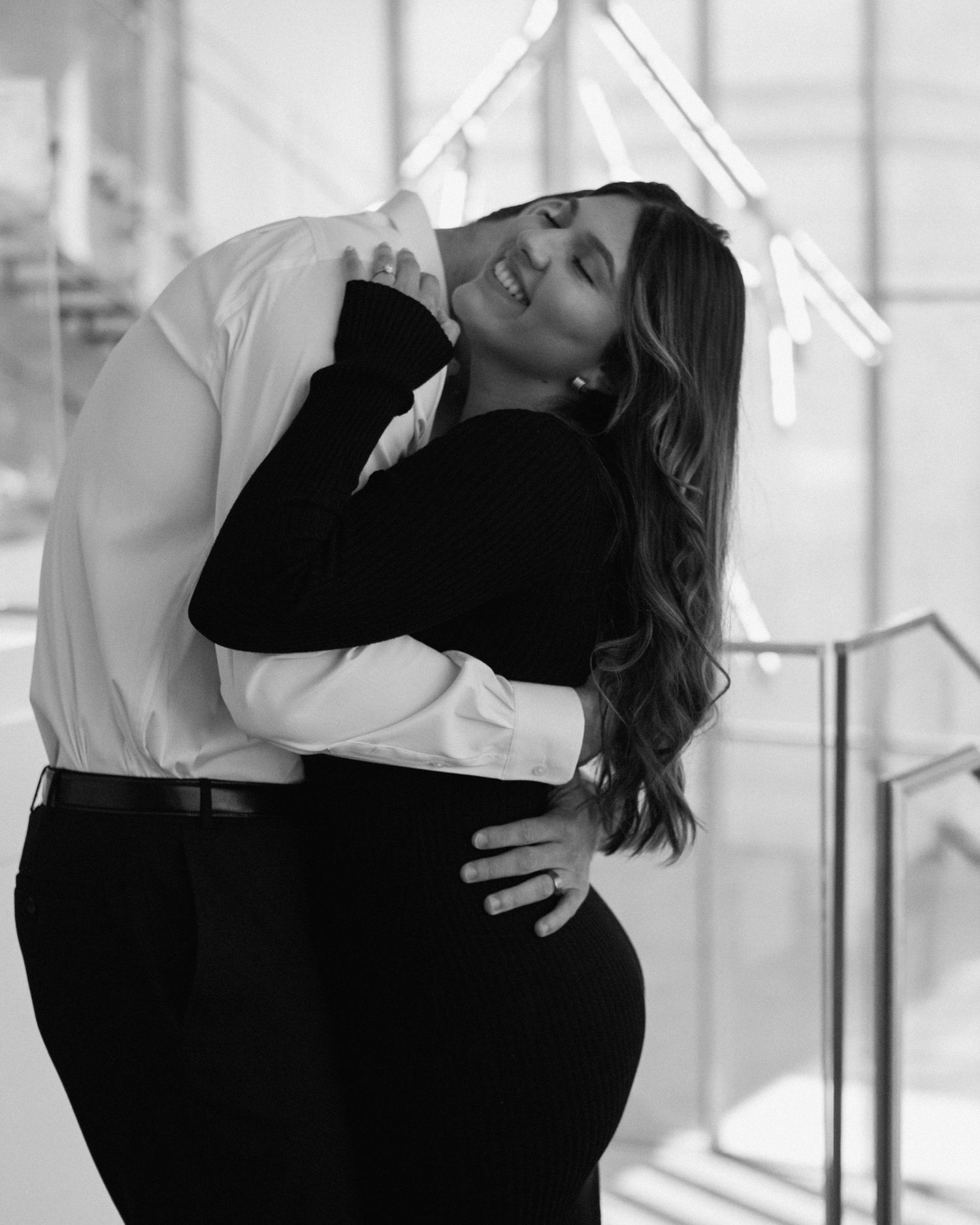 Elegant engaged couple smiling and embracing in downtown Louisville, with the woman showing her engagement ring
