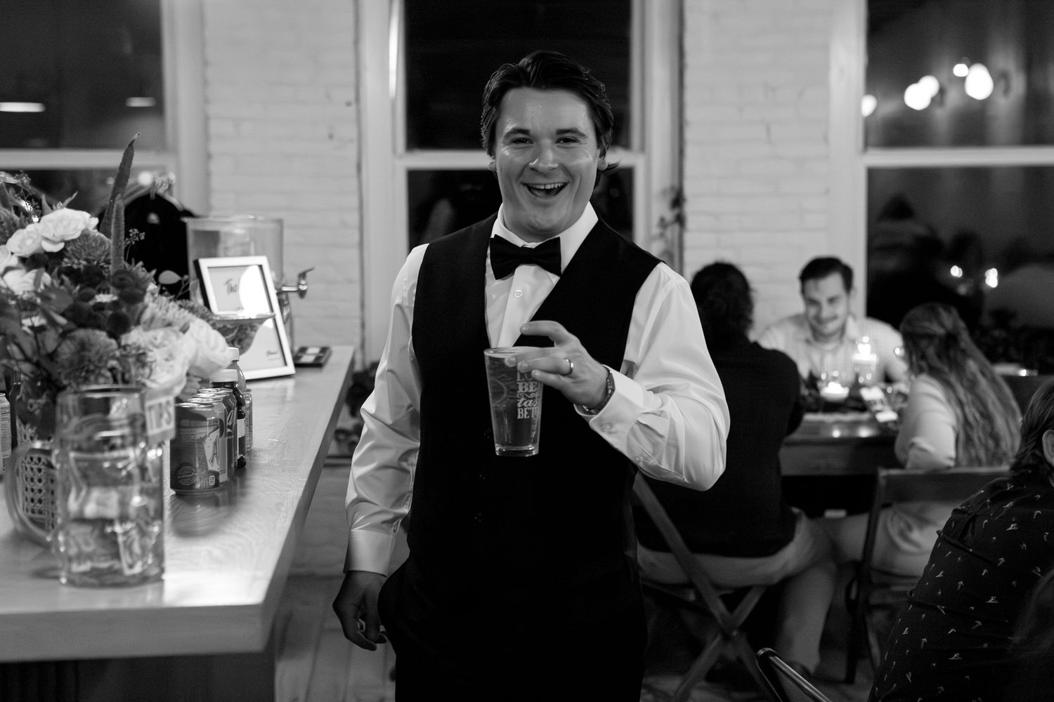 A person in formal wait staff attire holds up a drink at an evening reception.
