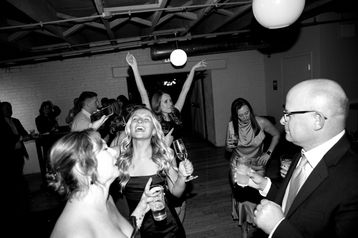 Black and white photo of guests celebrating and dancing at an indoor party with globe lights.