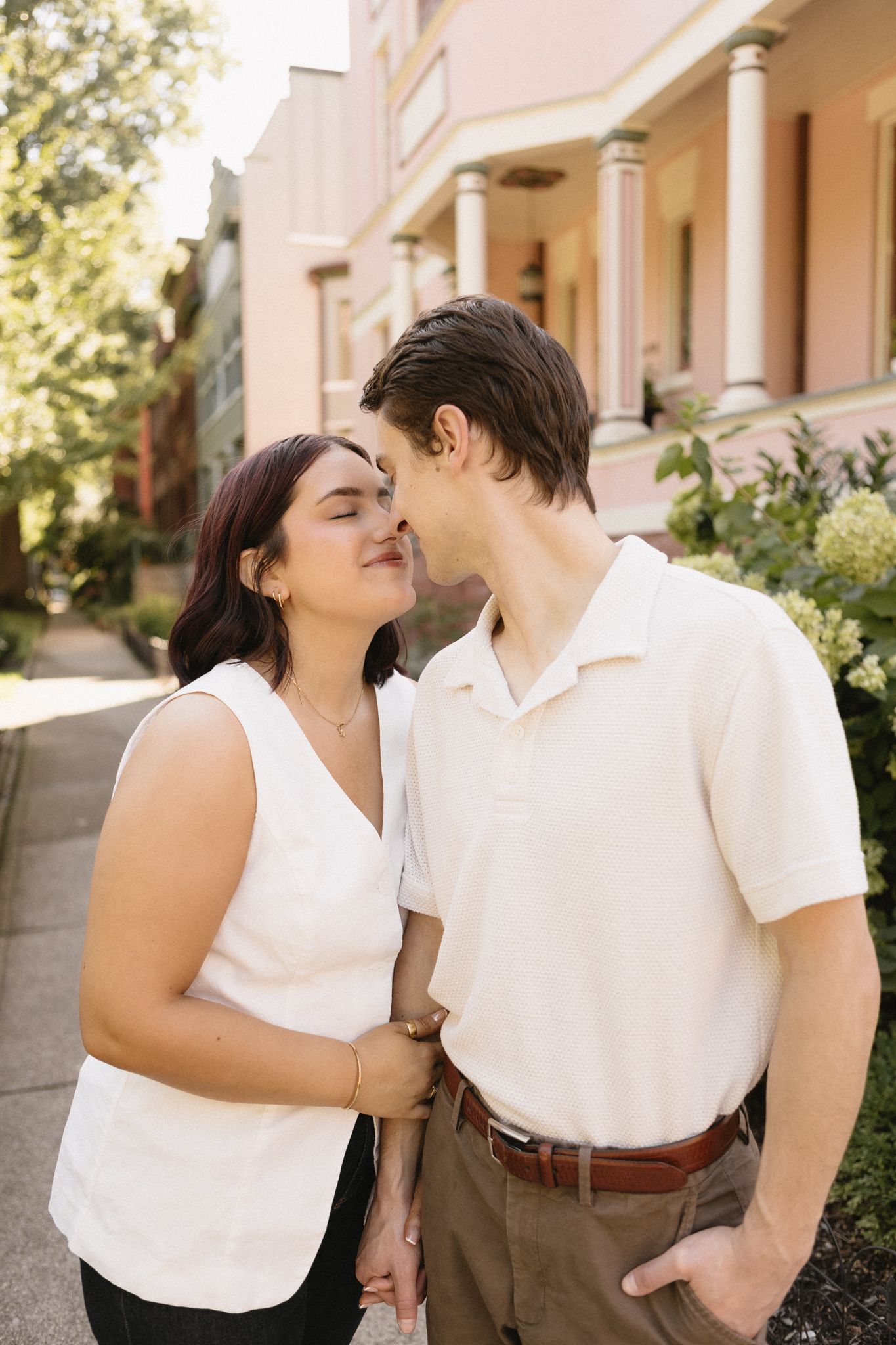 A couple wearing white tops shares tender moments in a series of romantic outdoor photos against a building exterior.