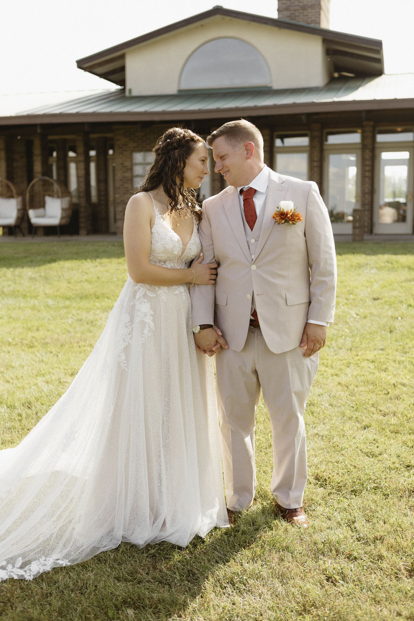 A romantic wedding portrait of a couple in formal attire standing on grass with a building in the background.